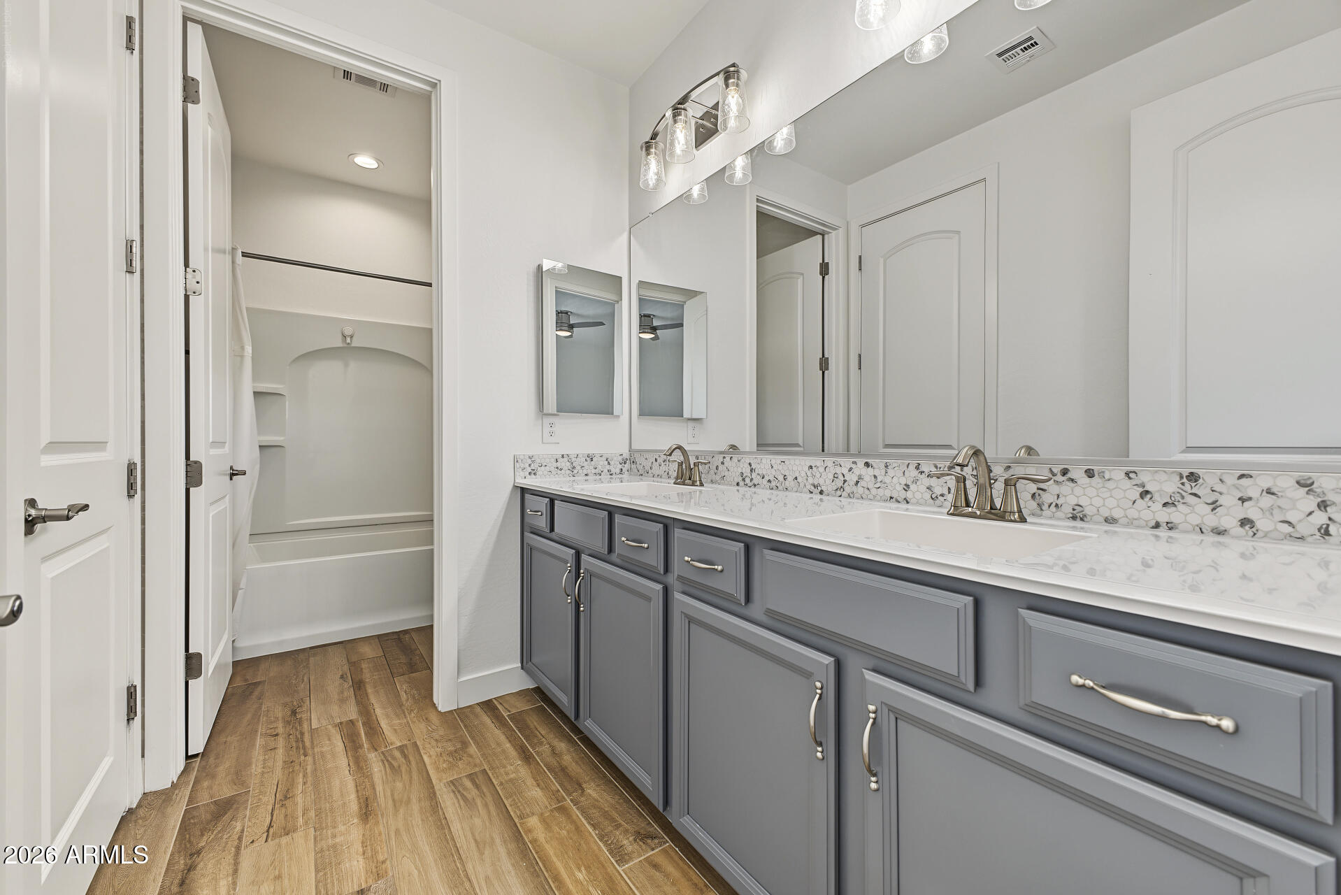 Bathroom with a gray double-sink vanity and a bathtub in the adjoining alcove.