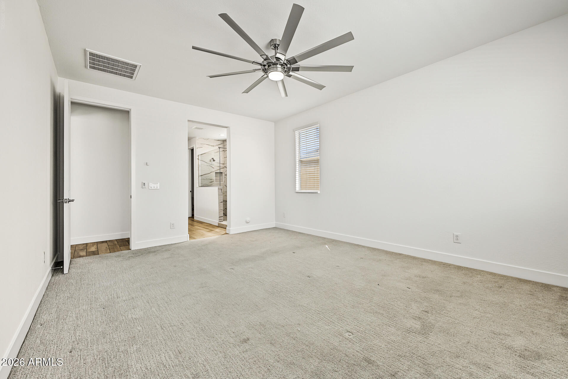 Empty carpeted bedroom with a modern ceiling fan and an open doorway to a tiled bathroom.