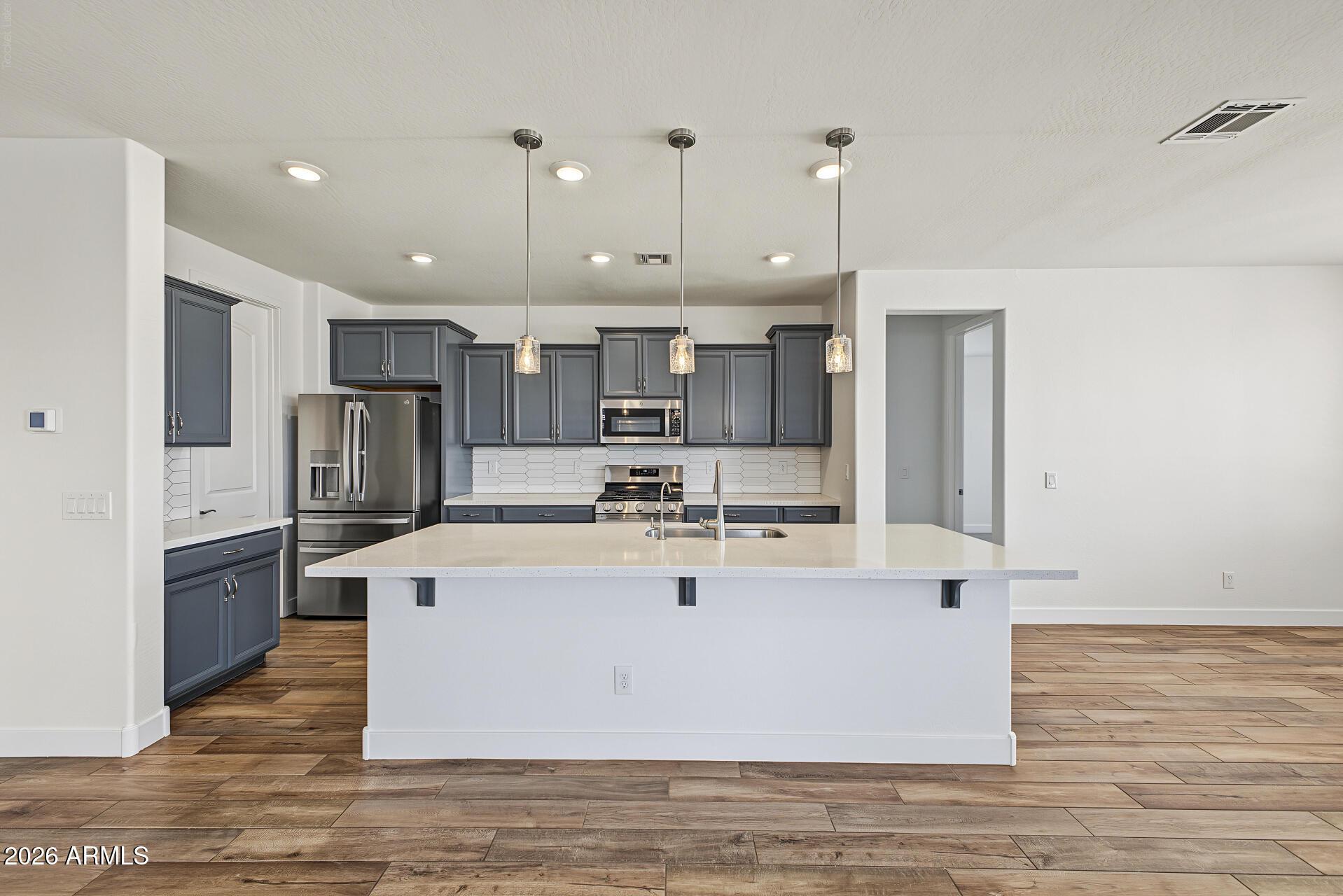 Kitchen with a large white island, dark cabinetry, stainless steel appliances, and geometric tile backsplash.