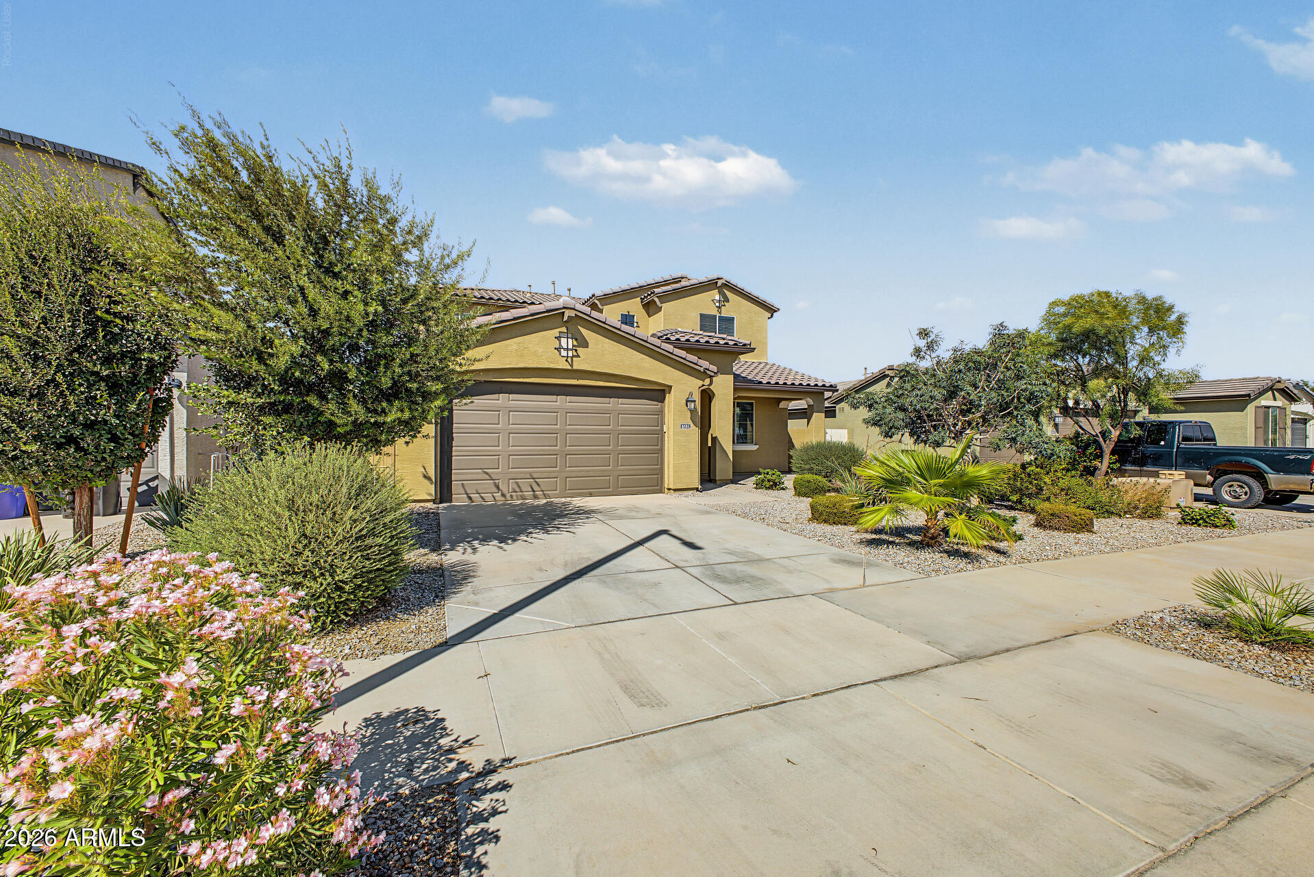 Tan stucco home with a two-car garage, broad driveway, and desert landscaping.