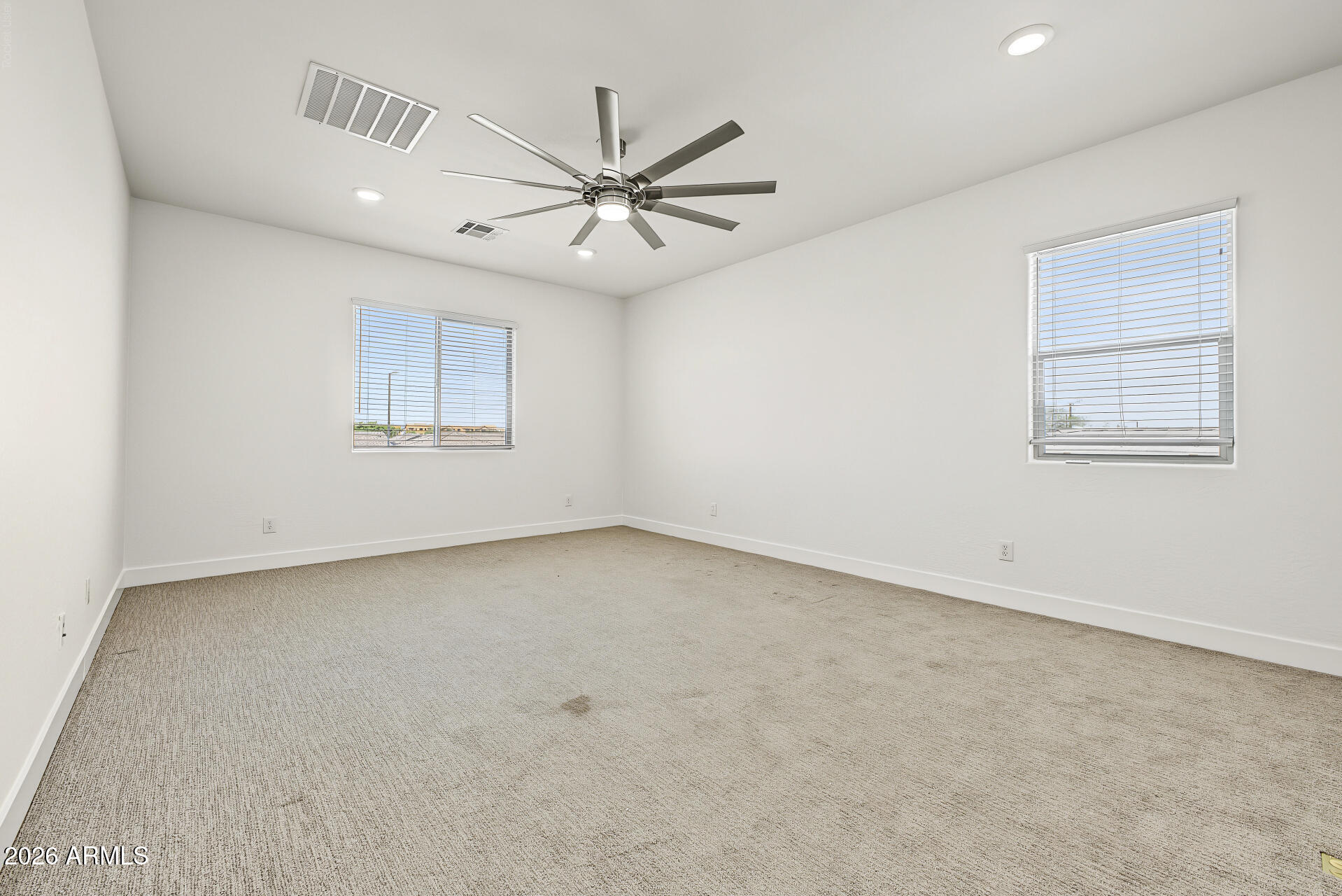 Empty carpeted bedroom with two windows and a ceiling fan.