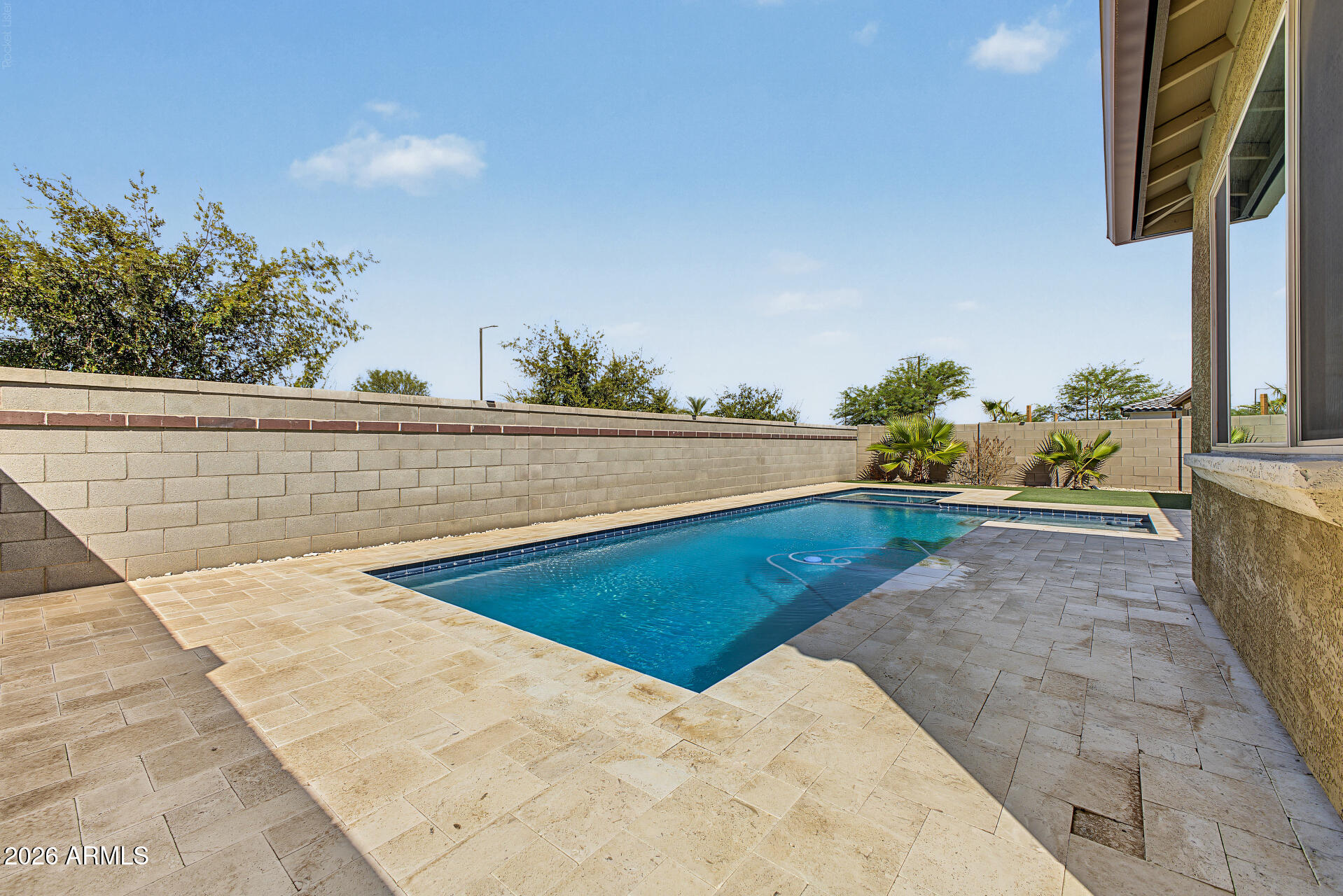 Backyard swimming pool with a broad paver deck and block privacy walls.