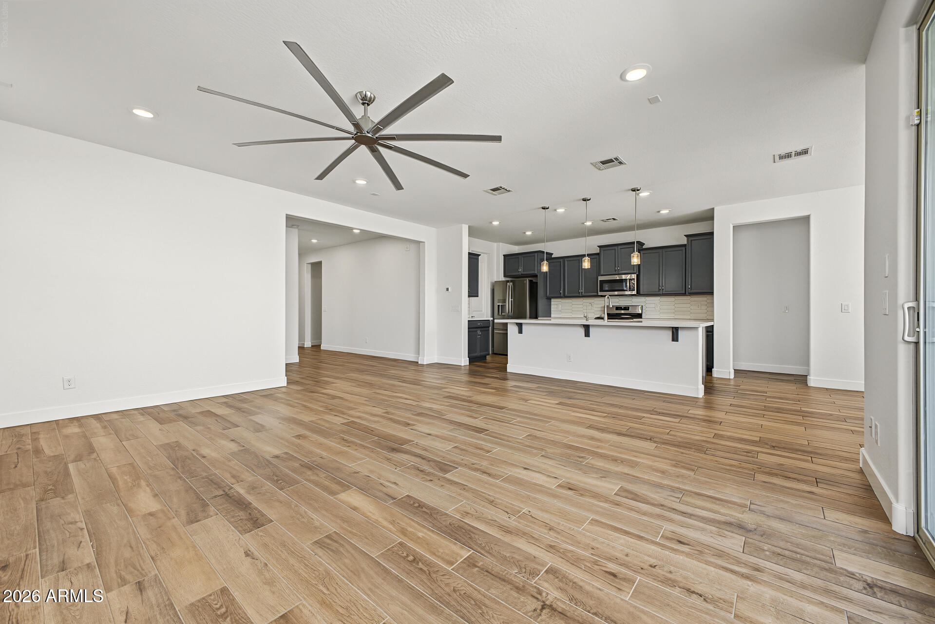 Open living area and kitchen with wood-look tile floors, dark cabinets, and a long breakfast-bar island.
