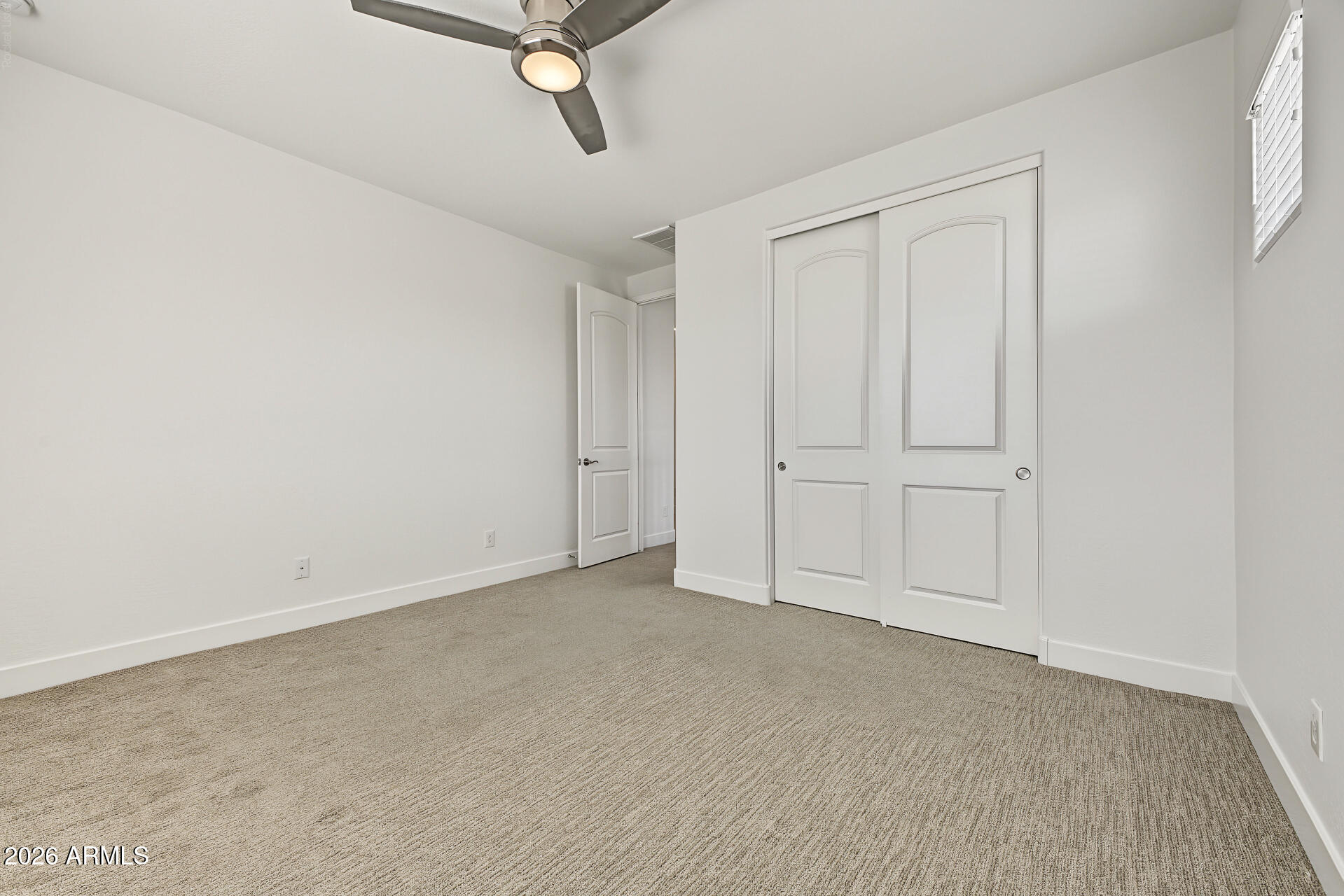 Empty carpeted bedroom with white sliding closet doors and a ceiling fan.