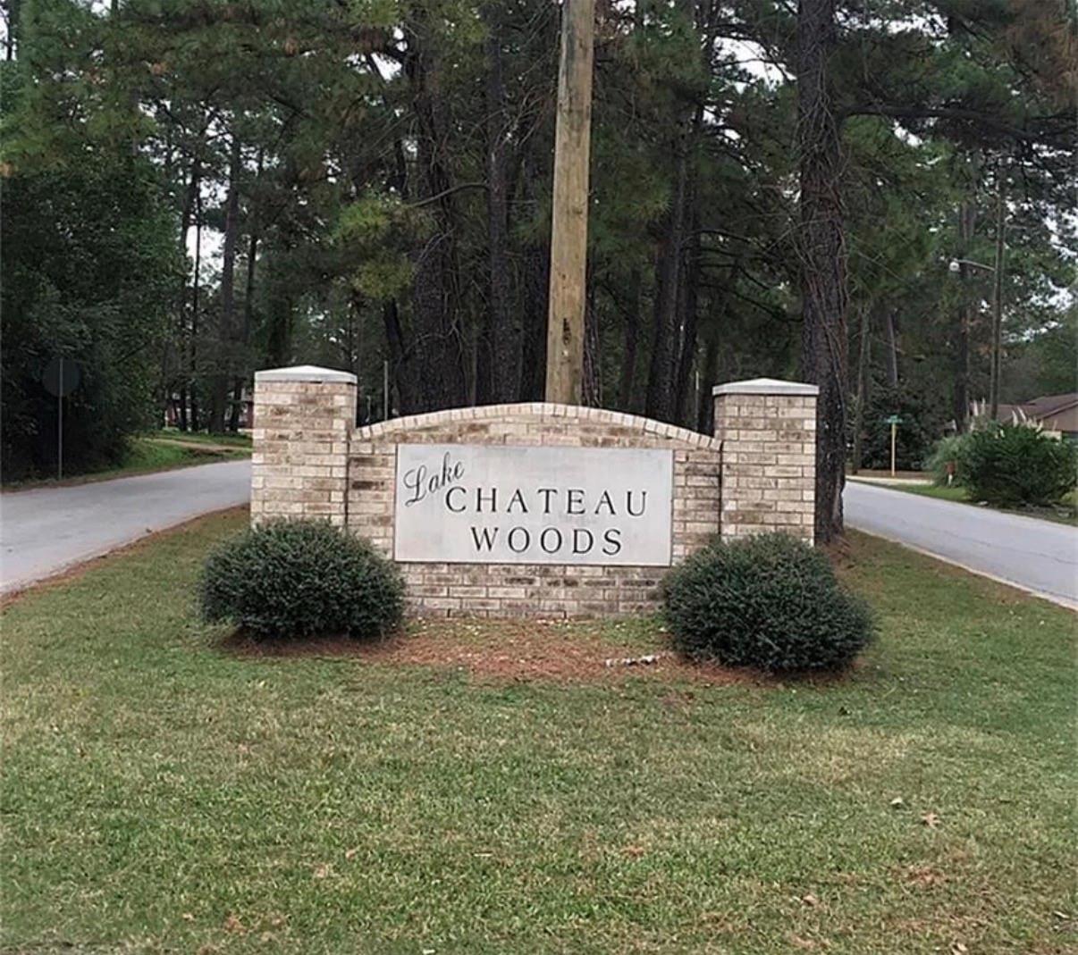 Lake Chateau Woods neighborhood entrance sign on a brick monument beside a tree-lined road.