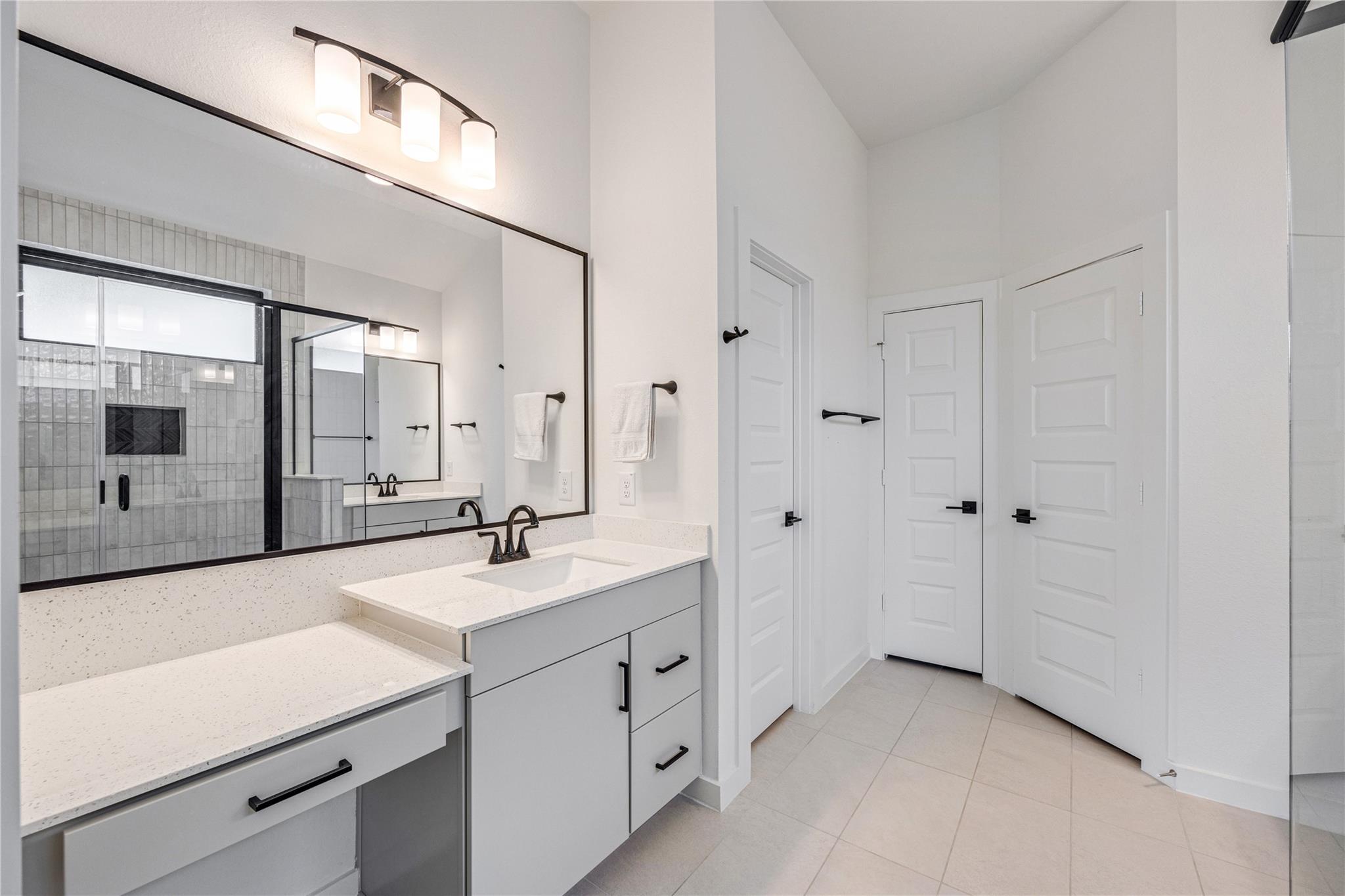 Modern bathroom with a long white vanity, black-framed mirrors, and a glass-enclosed tiled shower.