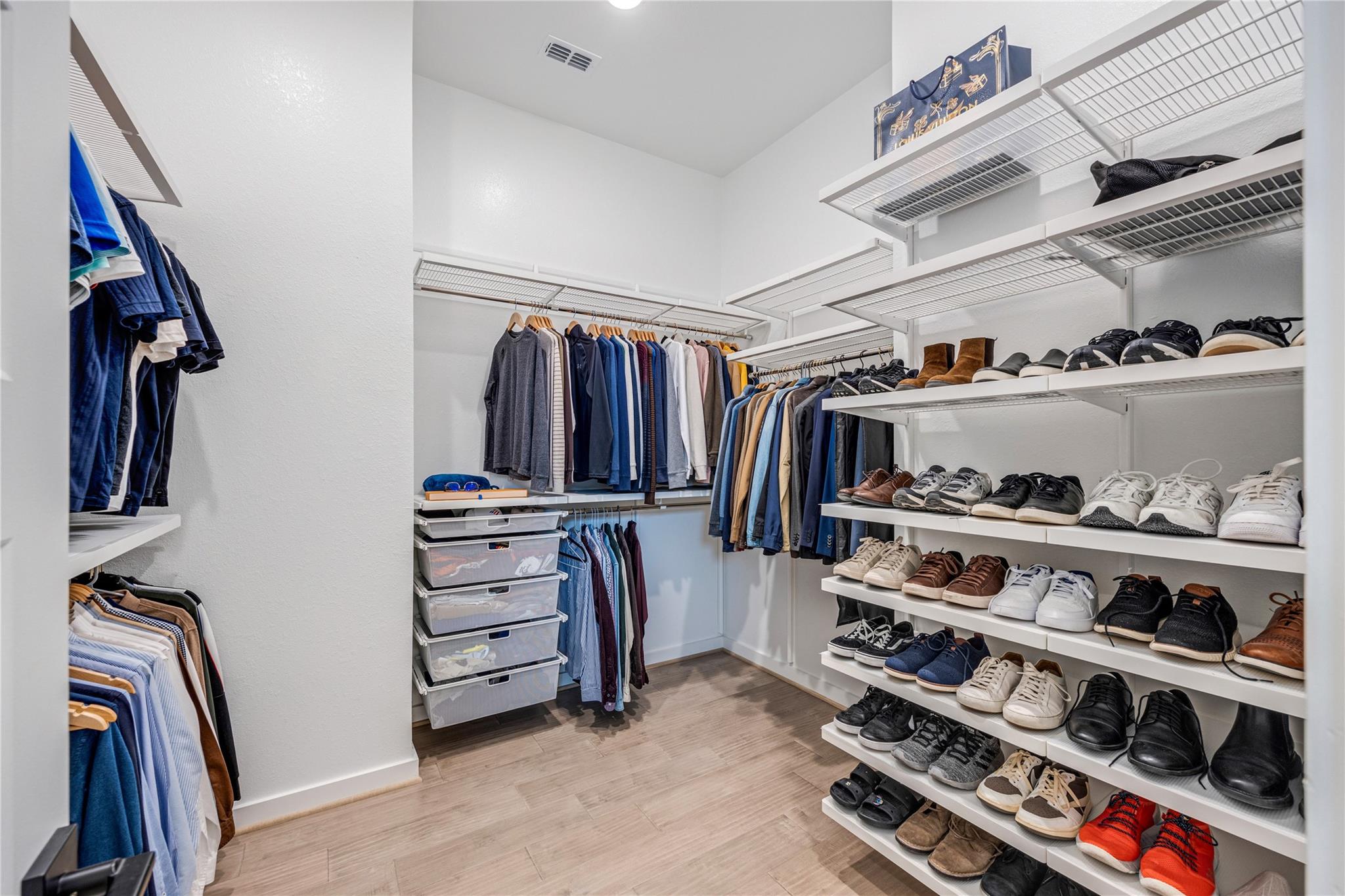 Walk-in closet with organized clothing, multiple shoe shelves, and clear storage drawers.
