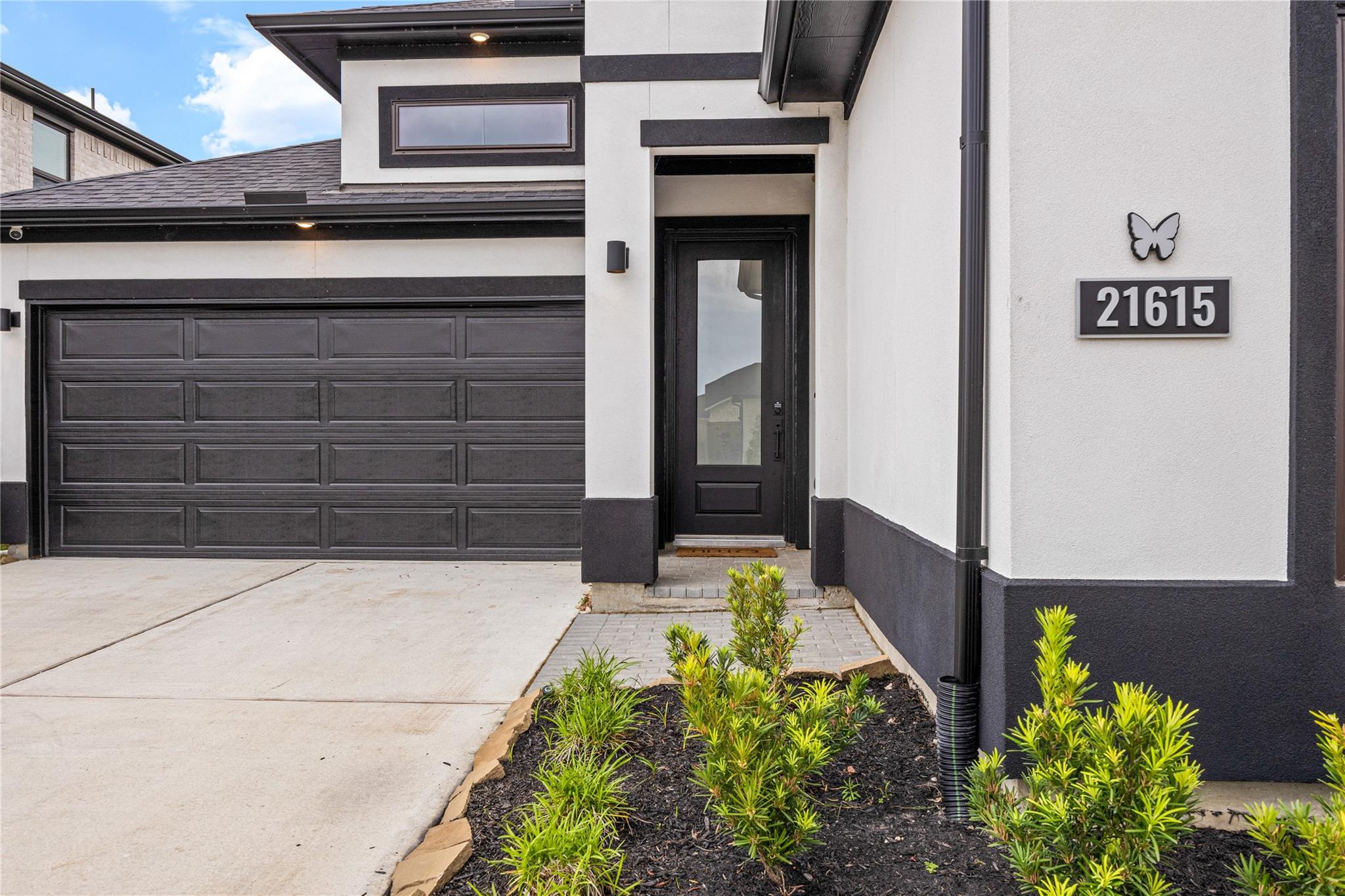 Modern home entrance with charcoal garage door, glass front door, and landscaped shrubs.