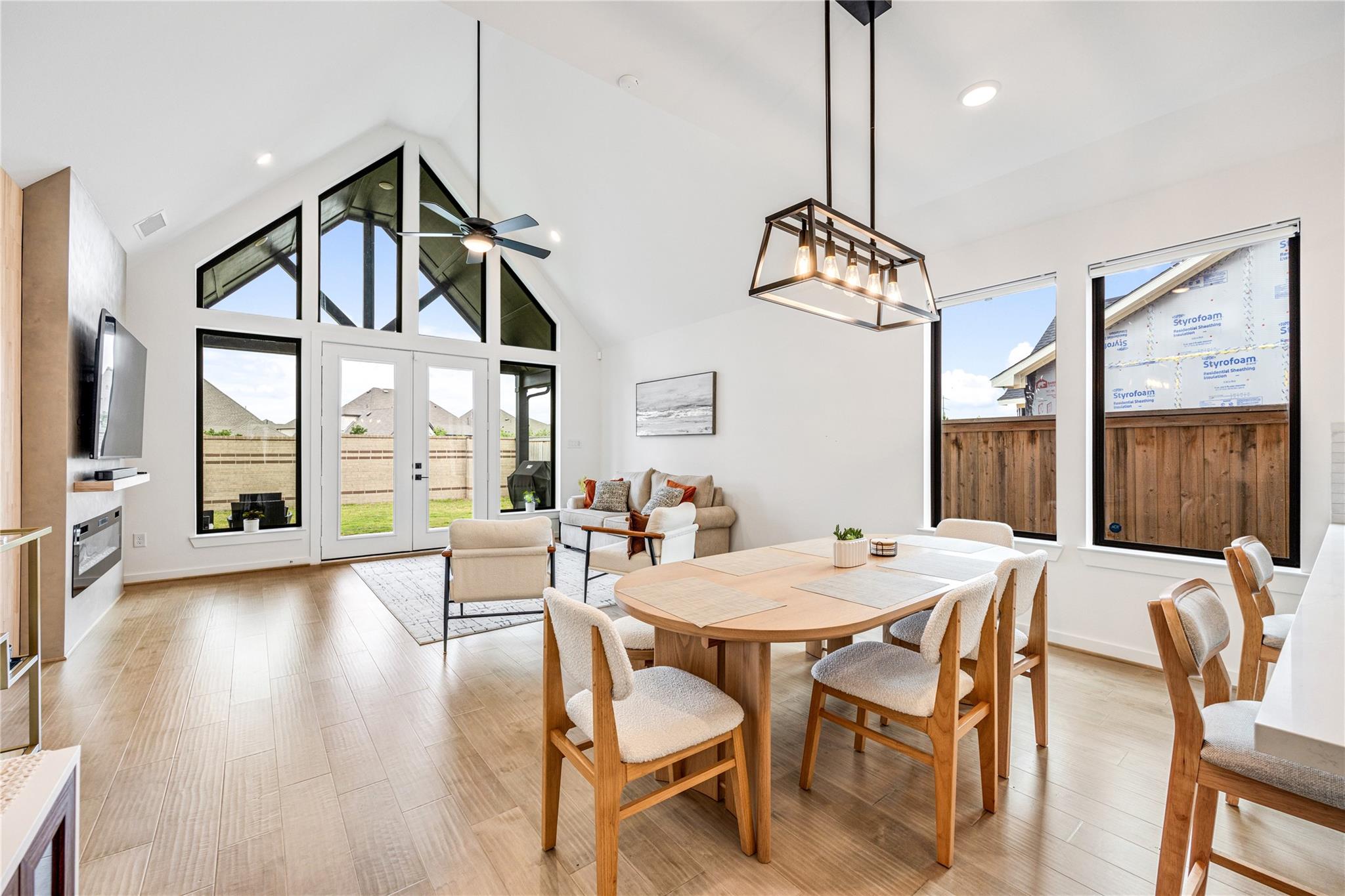Open living and dining room with vaulted ceiling, tall triangular windows, and a wood dining table.