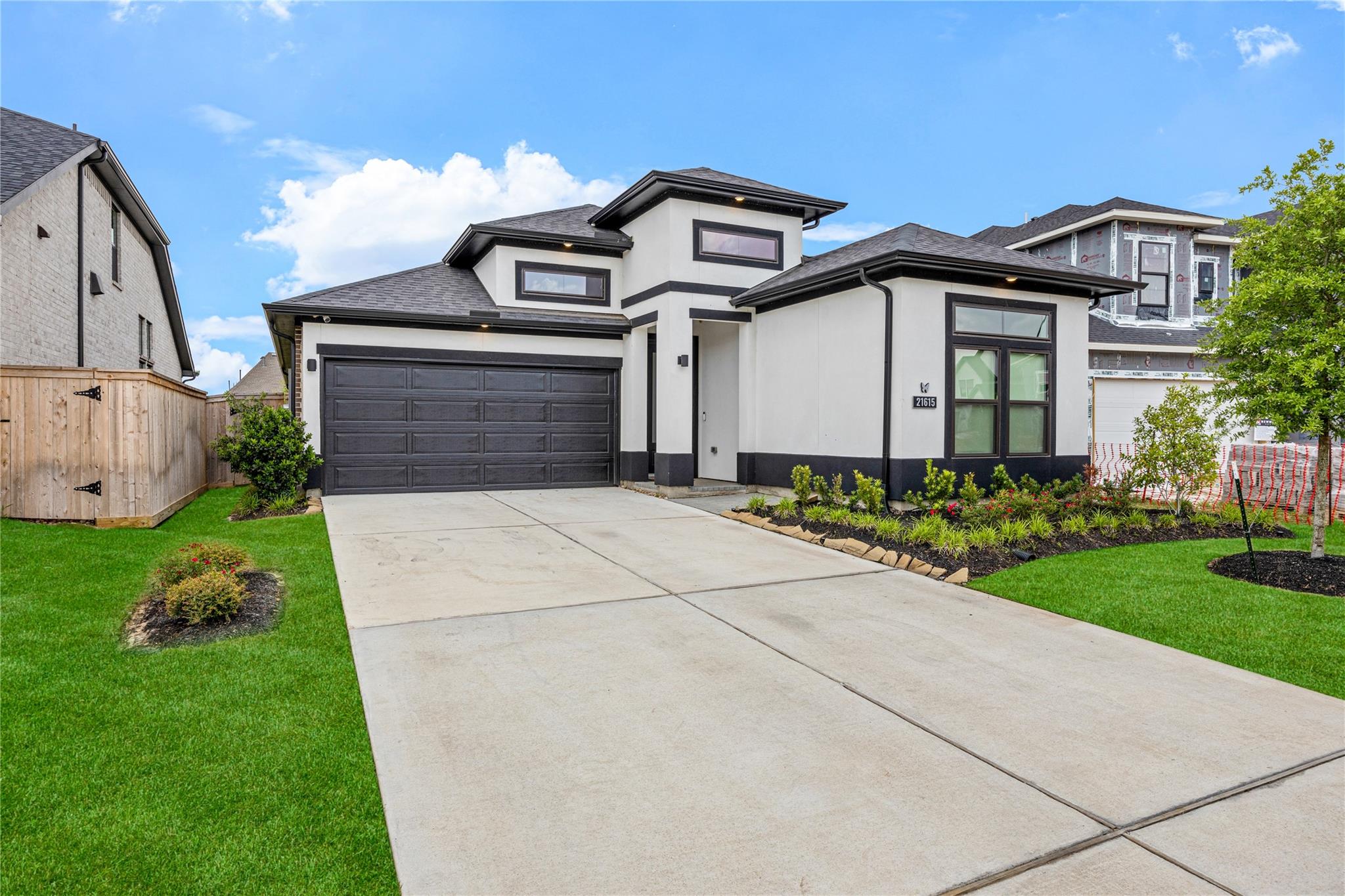 Modern white house with black trim, a dark double garage door, and a wide concrete driveway.