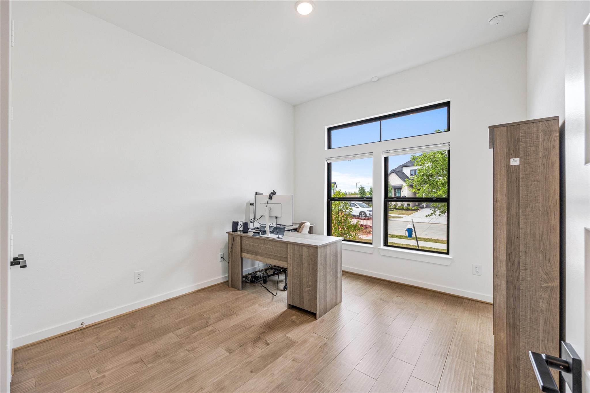 Home office with a computer desk, wood-look tile floors, and tall windows overlooking the street.