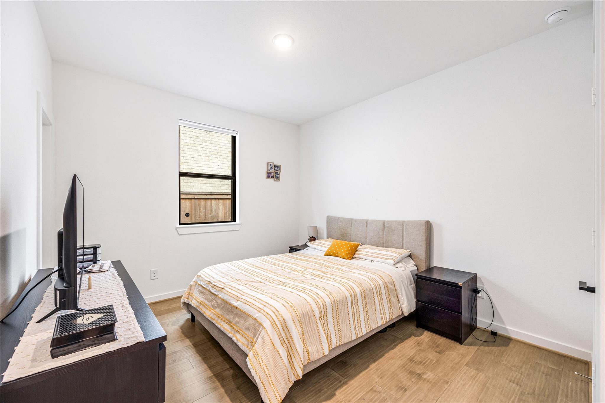 Bedroom with mustard-striped bedding, dark wood nightstands, and wood-look flooring.