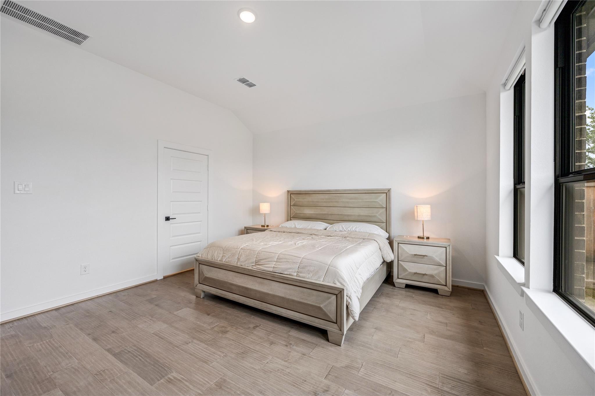 Furnished bedroom with a large bed, matching bedside tables, and tall black-framed windows.