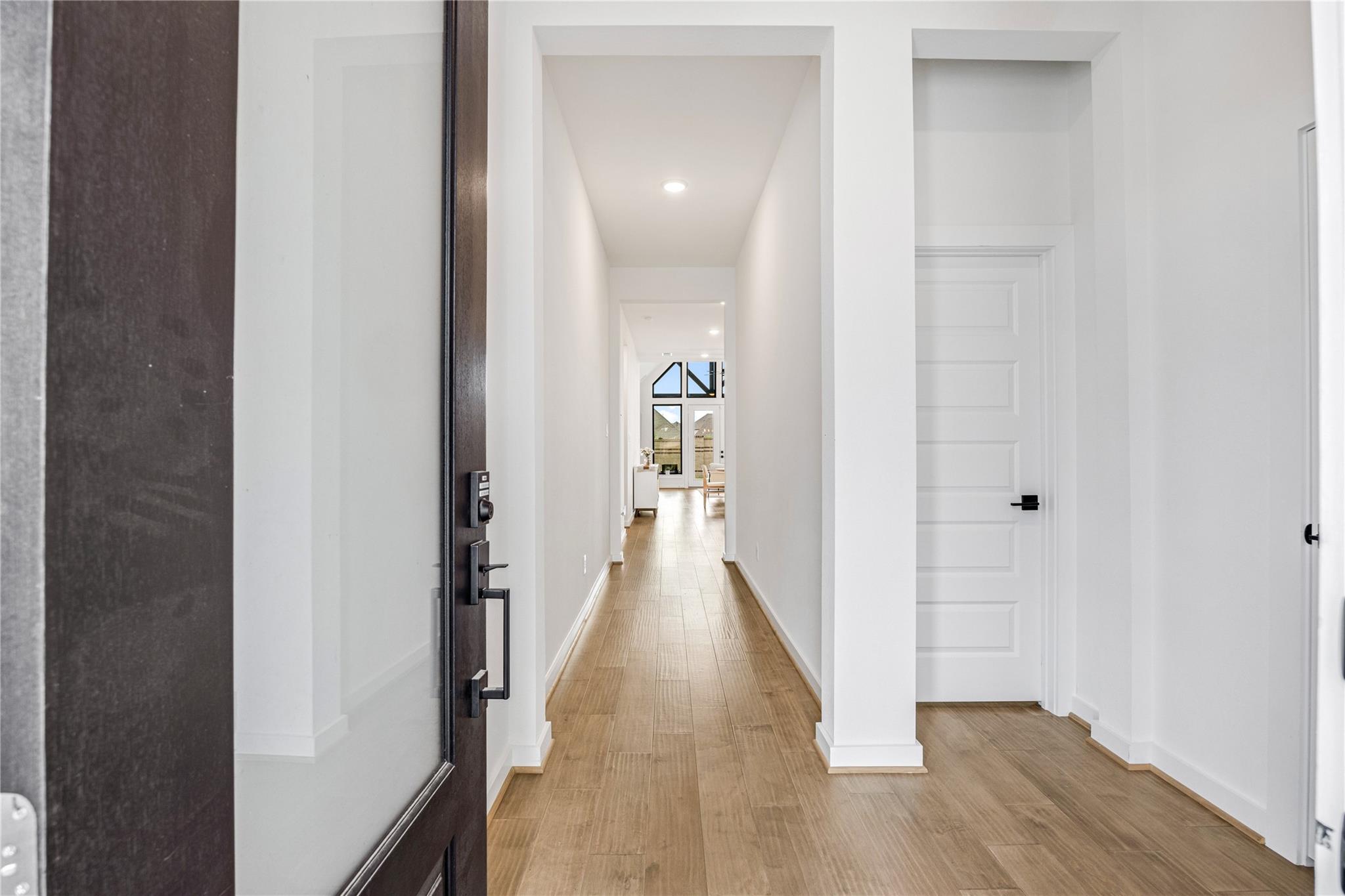 Bright entryway with a long wood-look tile hallway and an open dark front door.