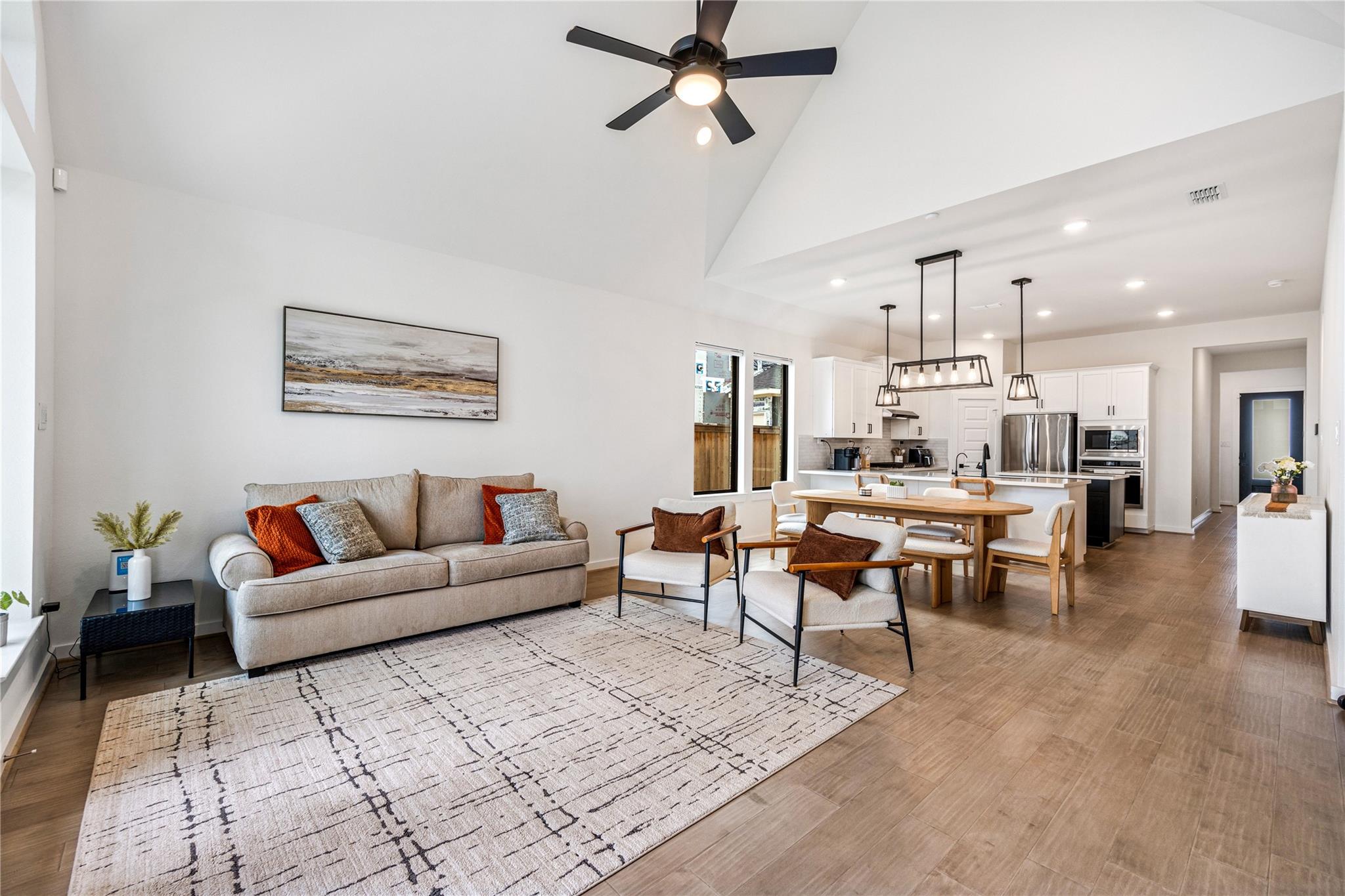 Open-plan living room and kitchen with a vaulted ceiling, neutral seating, and a wood dining table.