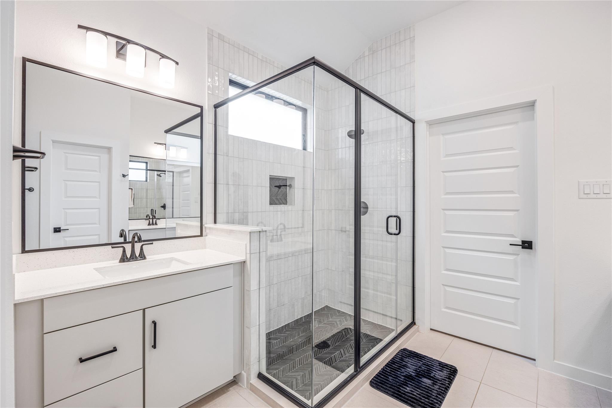 Modern bathroom with a glass-enclosed, dark-trimmed walk-in shower and white vanity.