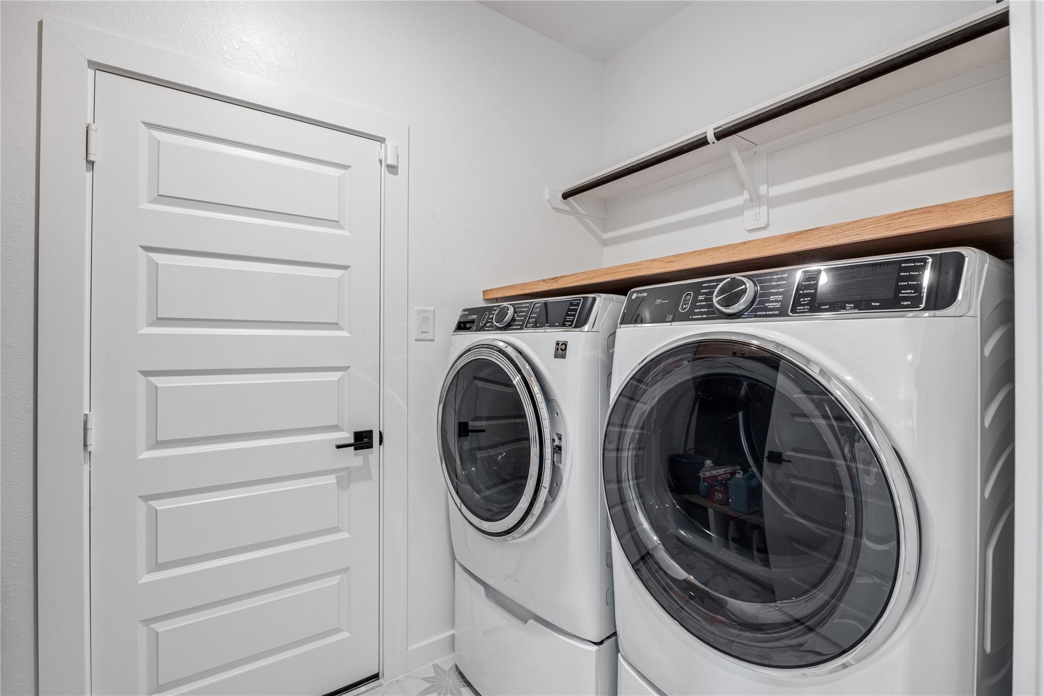 Laundry room with front-loading washer and dryer beneath a wood countertop and hanging rod.