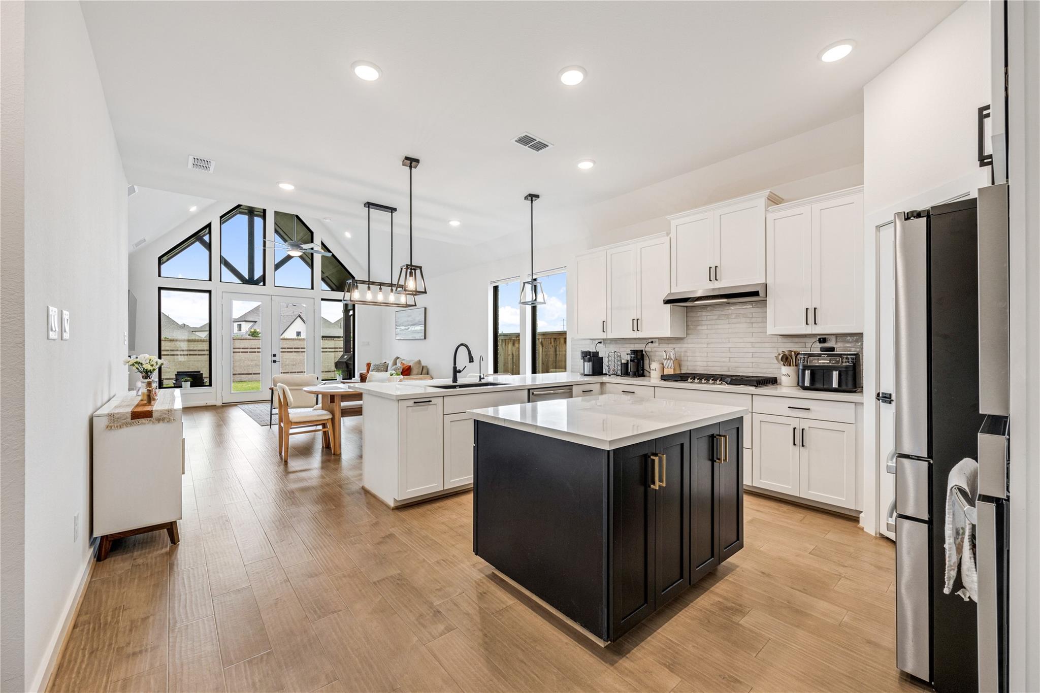 Open-concept kitchen with a large dark island, white cabinetry, and geometric windows.