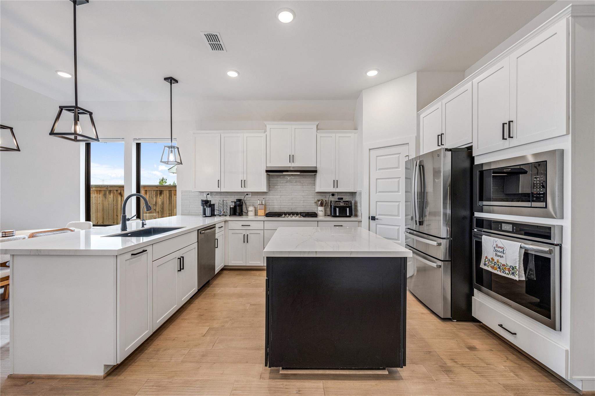 Modern kitchen with a large dark island, white shaker cabinets, and stainless steel appliances.