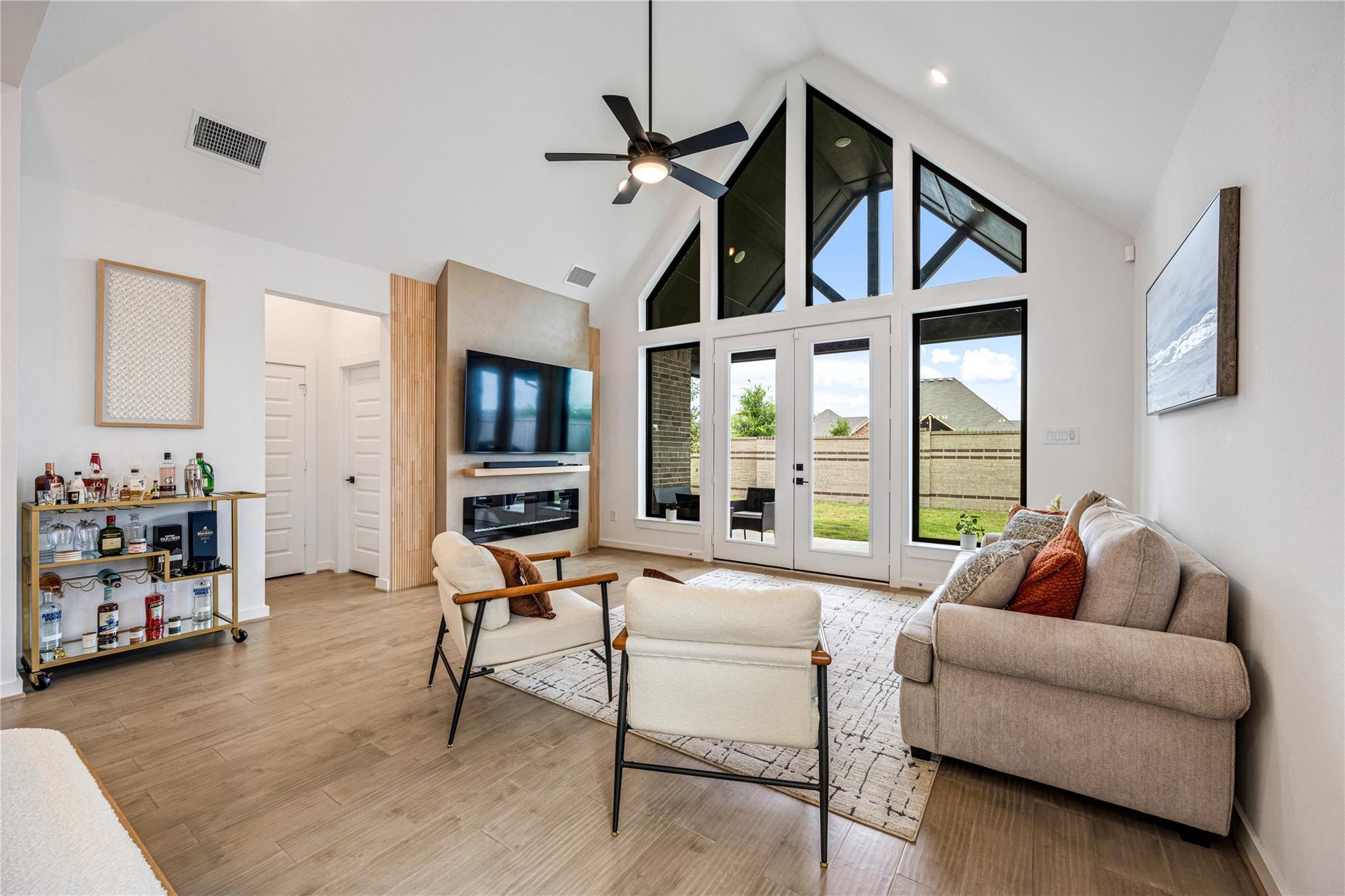 Vaulted living room with tall geometric windows, glass backyard doors, and a wall-mounted television above a fireplace.