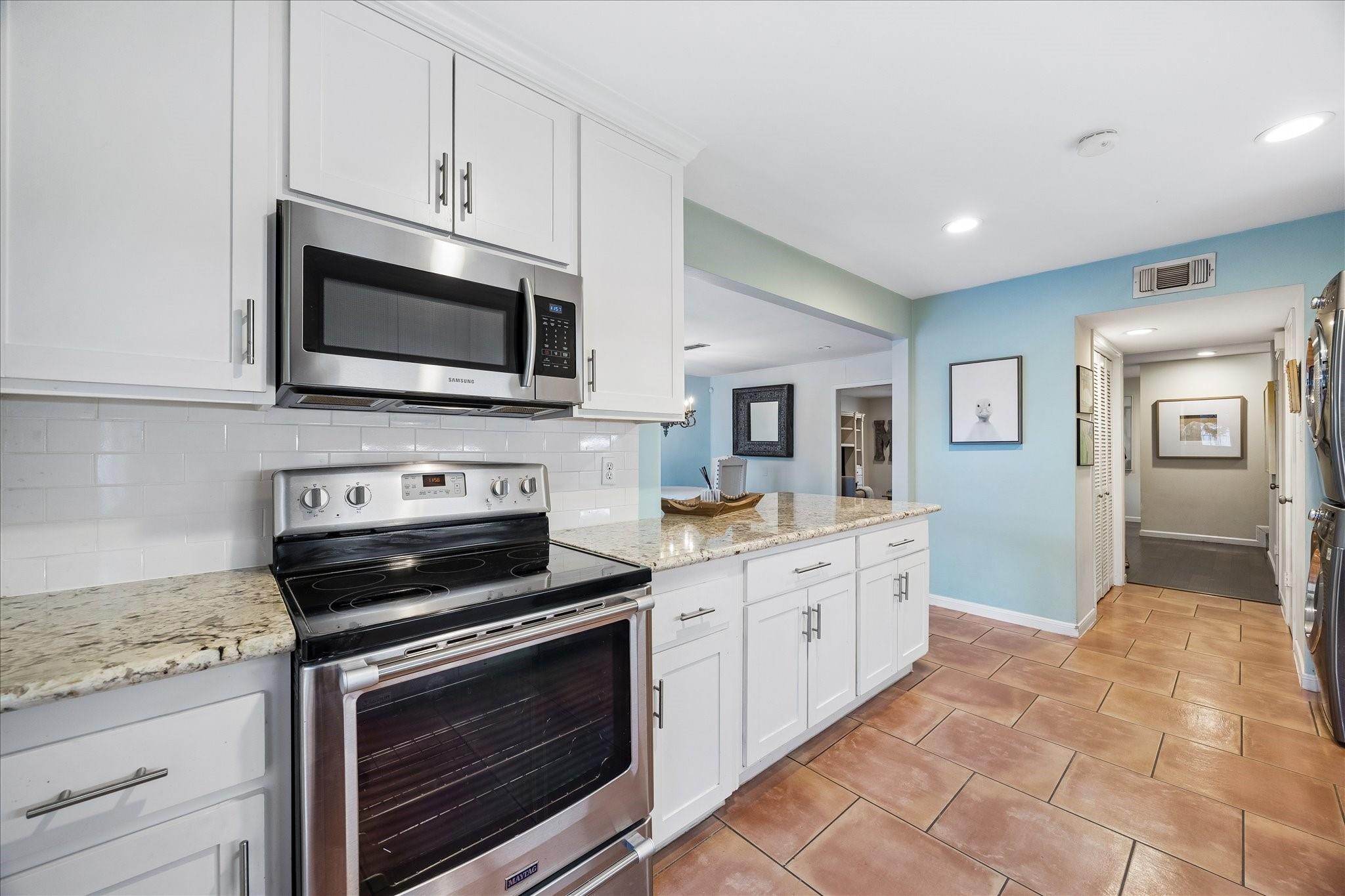 Kitchen with white cabinets, stainless steel appliances, granite counters, and terracotta tile flooring.