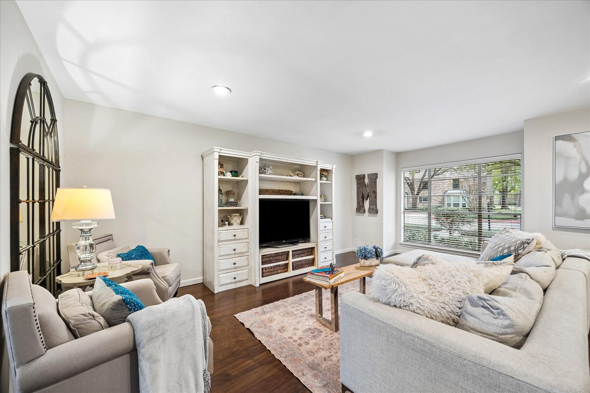 Living room with pale seating, a white built-in entertainment center, and a large window with blinds.