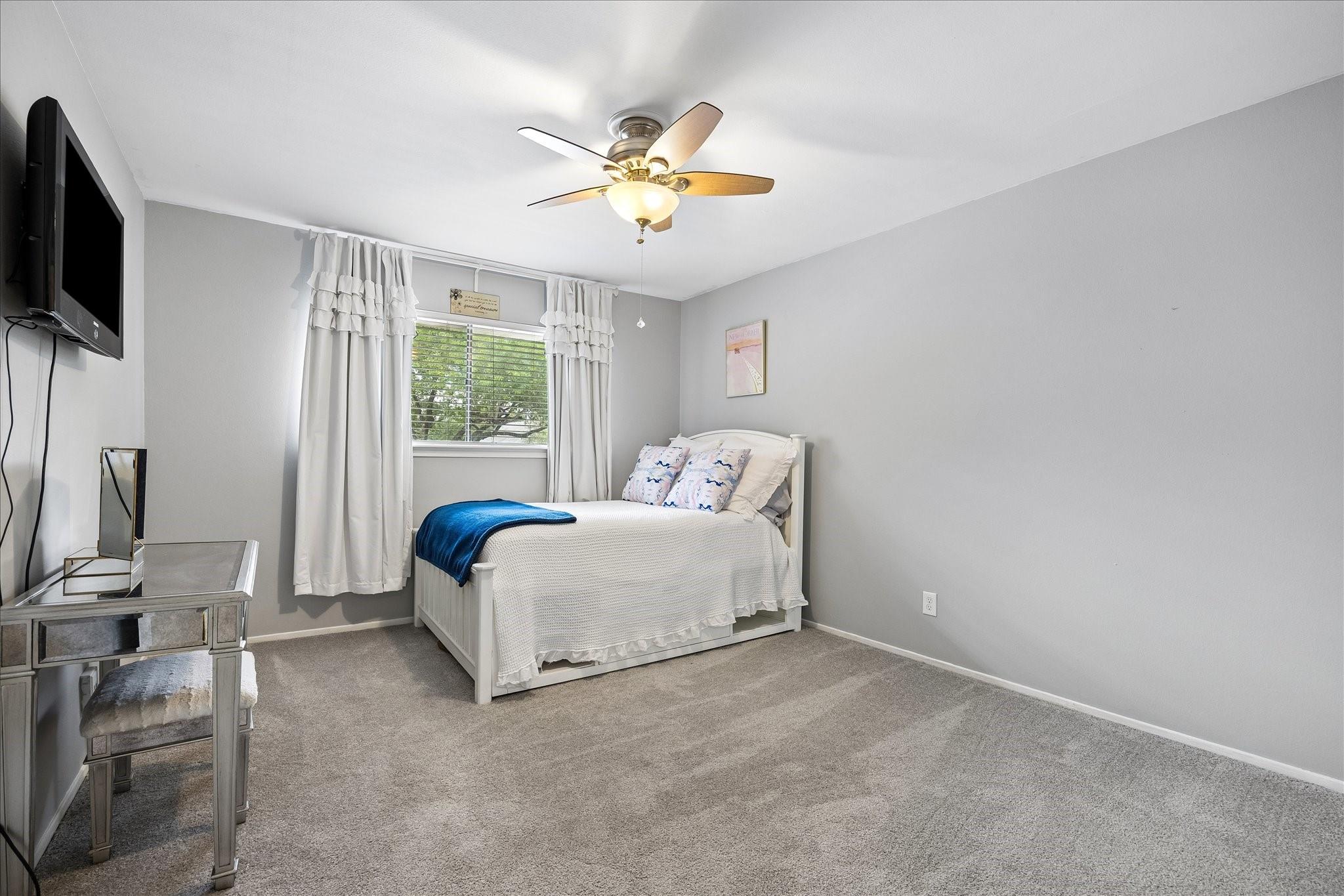 Furnished bedroom with a white bed, blue throw, gray carpet, and window with white curtains.