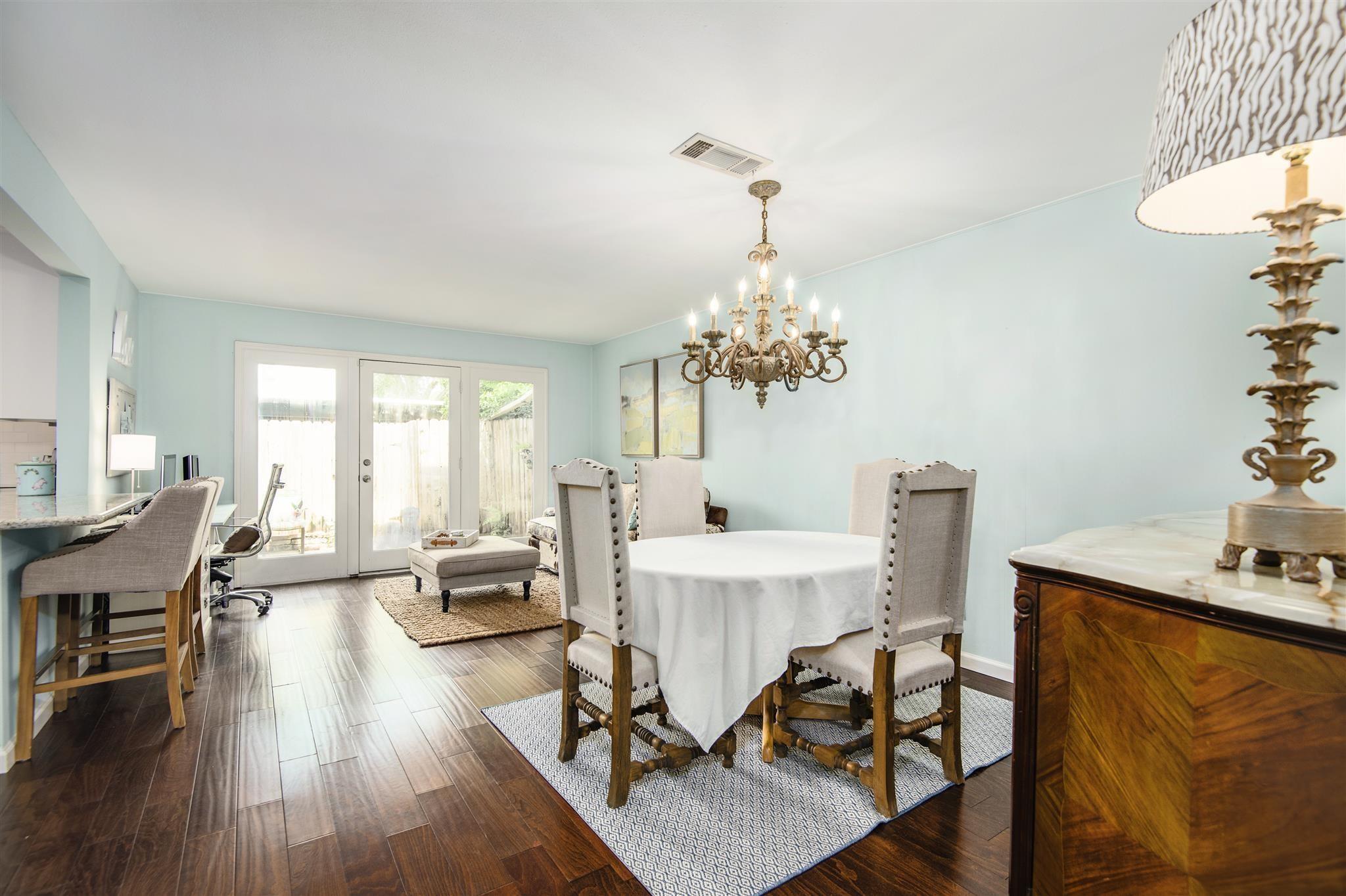 Dining area with a round table, upholstered chairs, ornate chandelier, and glass doors to a fenced patio.