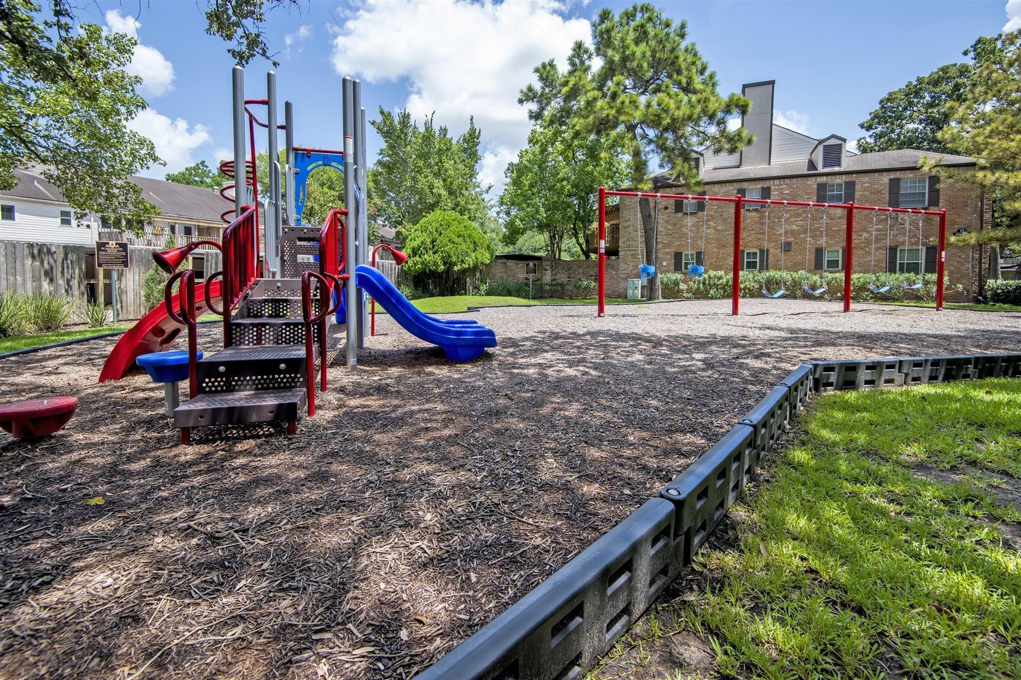 Community playground with colorful slides, climbing equipment, and swings on a wood-chip surface.