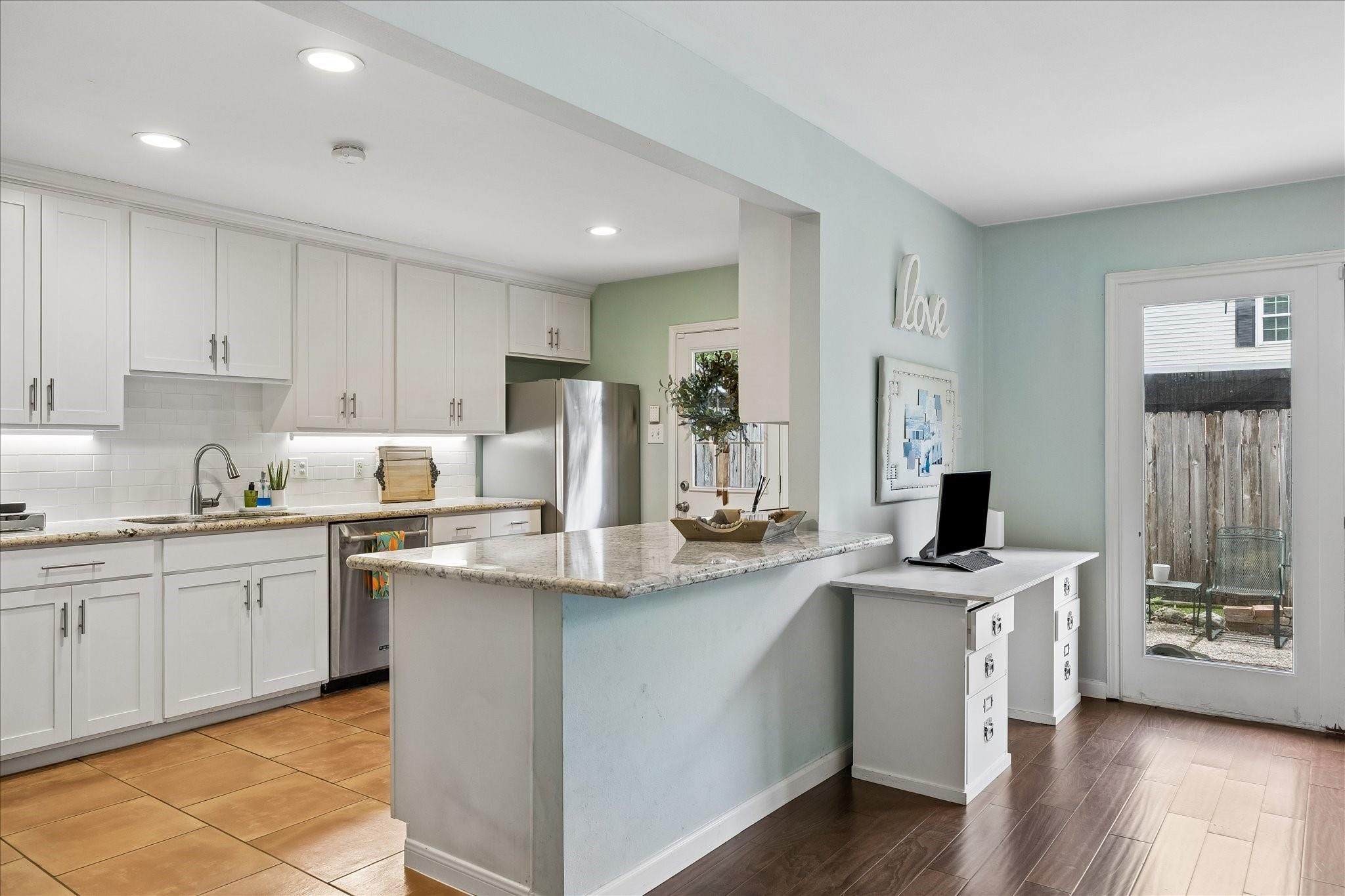 Kitchen with white cabinets, granite island, stainless appliances, and an adjoining desk area.