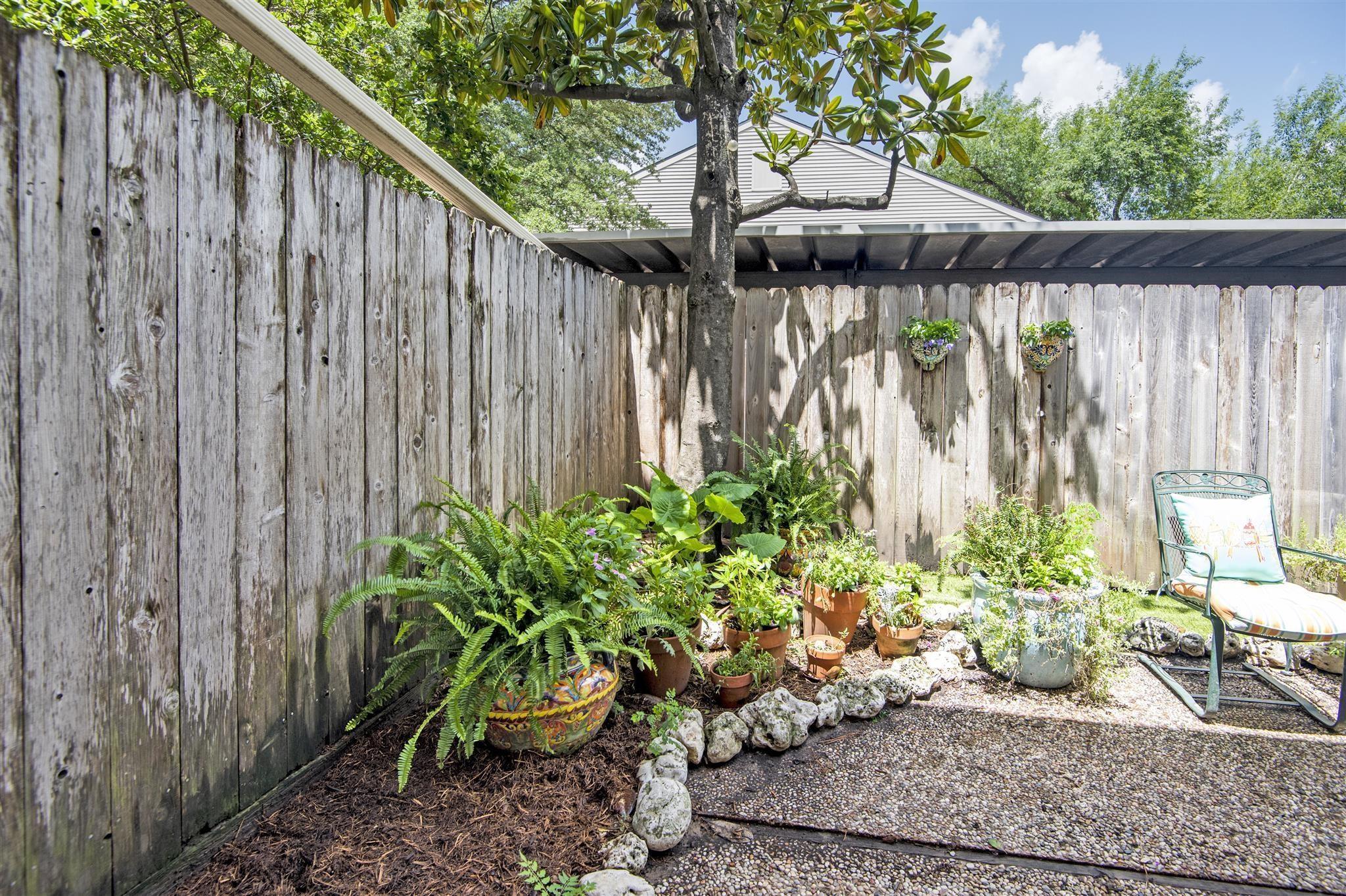 Fenced backyard patio with a lounge chair and leafy garden bed beneath a tree.