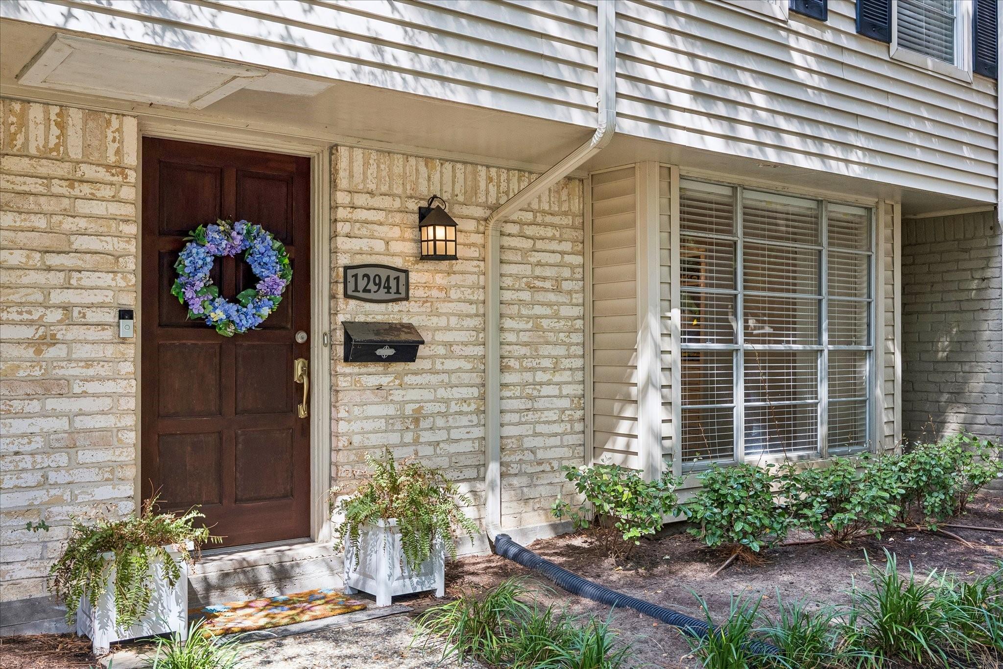 Home entrance with a dark wood door, blue floral wreath, light brick, and house number 12941.