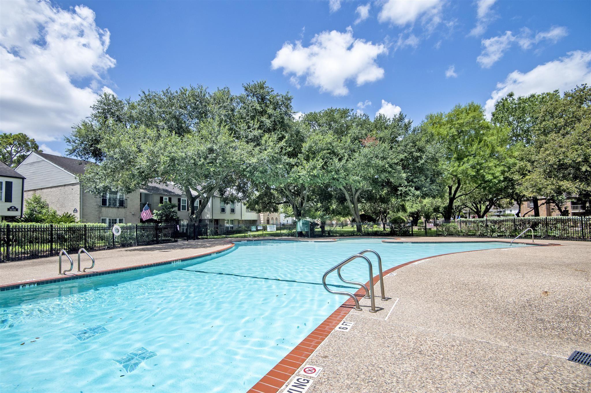 Outdoor swimming pool with a curved brick edge, metal ladders, and mature trees.