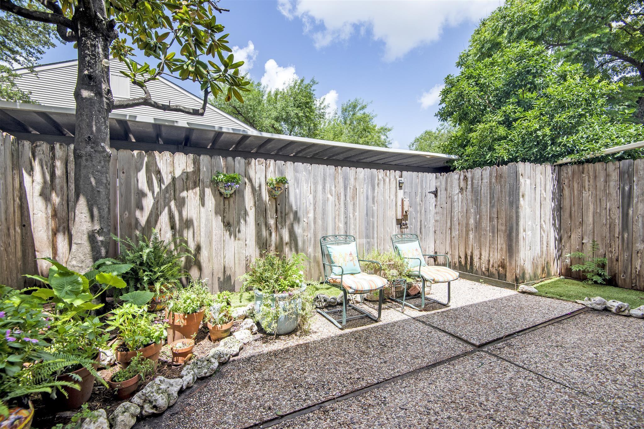 Private backyard patio with two cushioned chairs, potted plants, and a tall wooden fence.