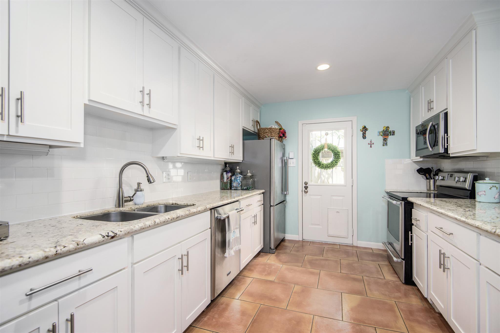 Kitchen with white cabinets, granite counters, stainless steel appliances, and terracotta-colored tile flooring.