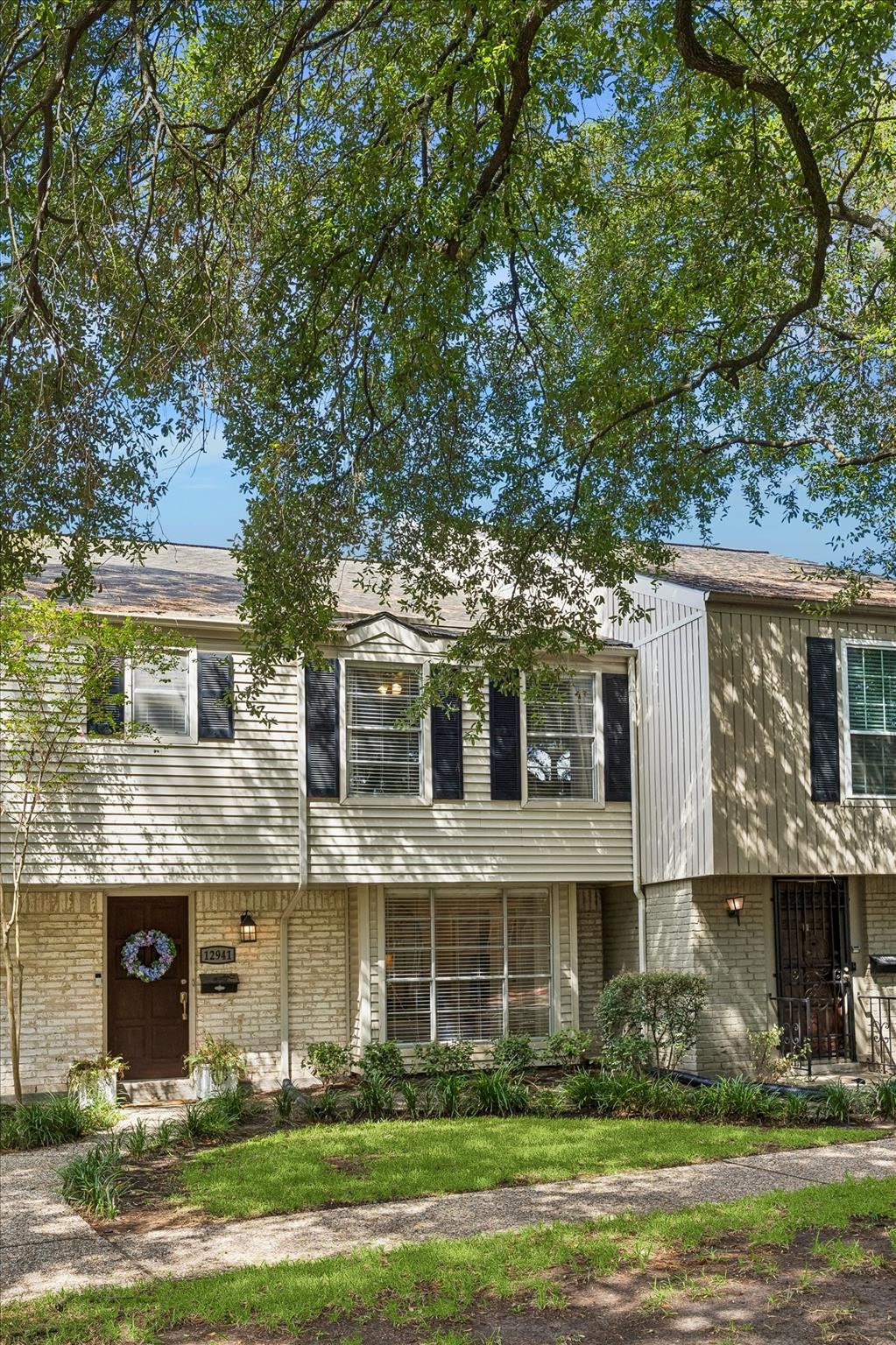 Two-story townhouse facade shaded by a mature tree, with pale brick and dark shutters.