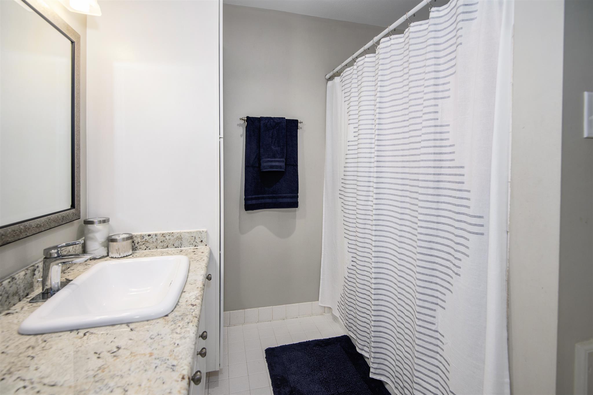 Bathroom with granite vanity, white sink, striped shower curtain, and navy towels.
