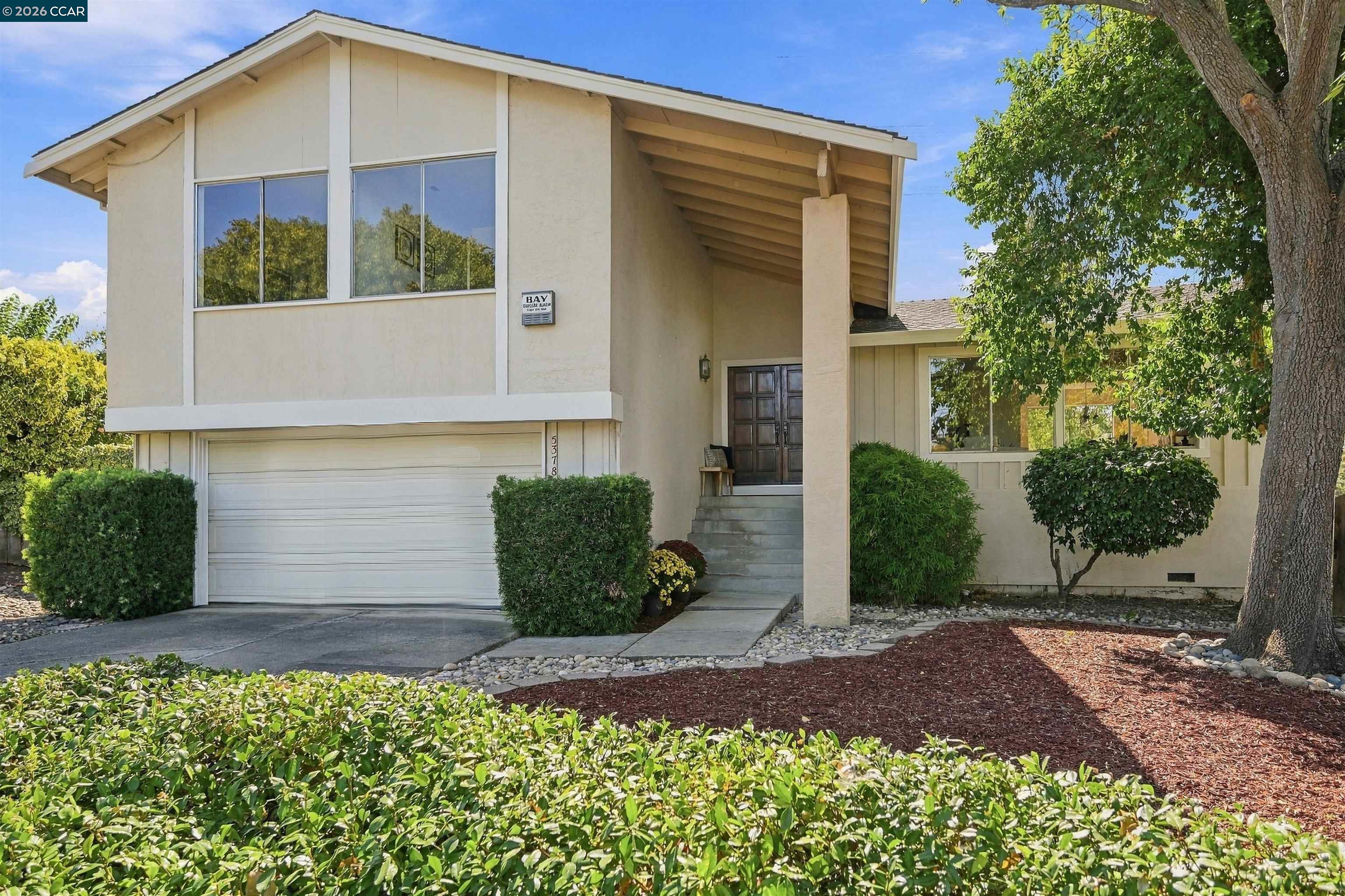 Two-story beige home with a two-car garage, recessed entry, and landscaped front yard.