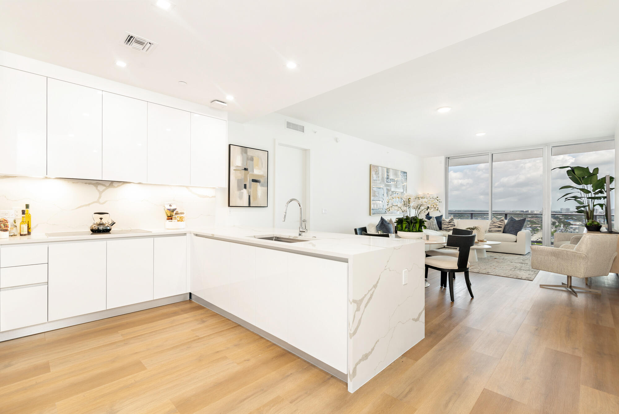 Open-plan kitchen with white stone island and living area overlooking West Palm Beach through large windows.