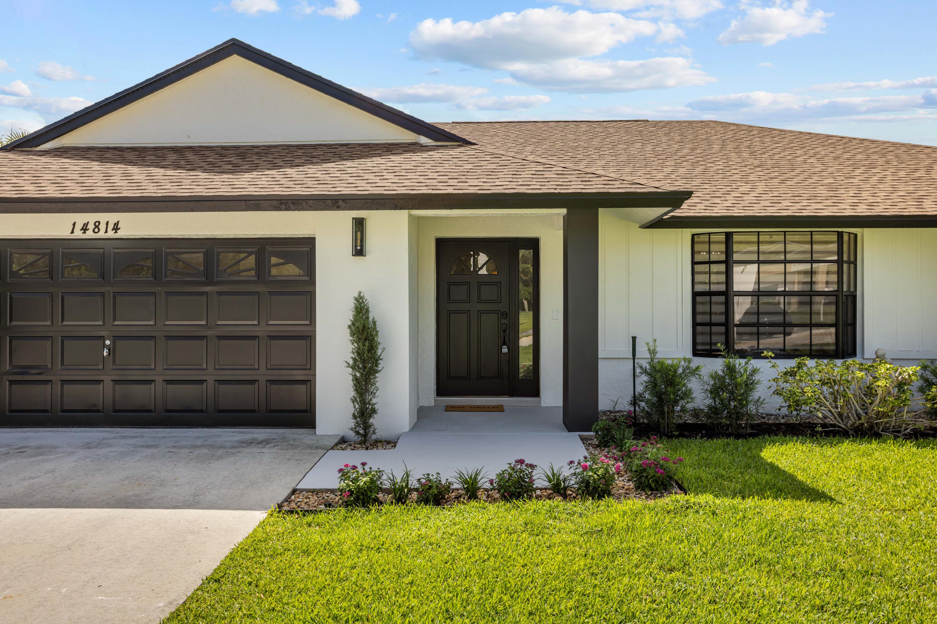 Single-story home with dark garage door, recessed entry, landscaped beds, and a green front lawn.