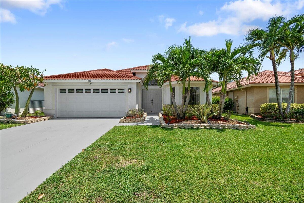 Single-story home with a red tile roof, wide garage, palm trees, and landscaped front lawn.