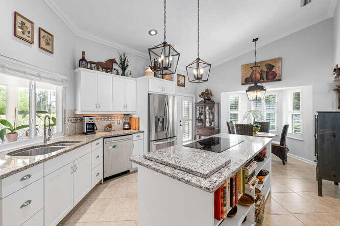 Bright kitchen with white cabinets, stainless steel appliances, and a large granite island with cooktop.