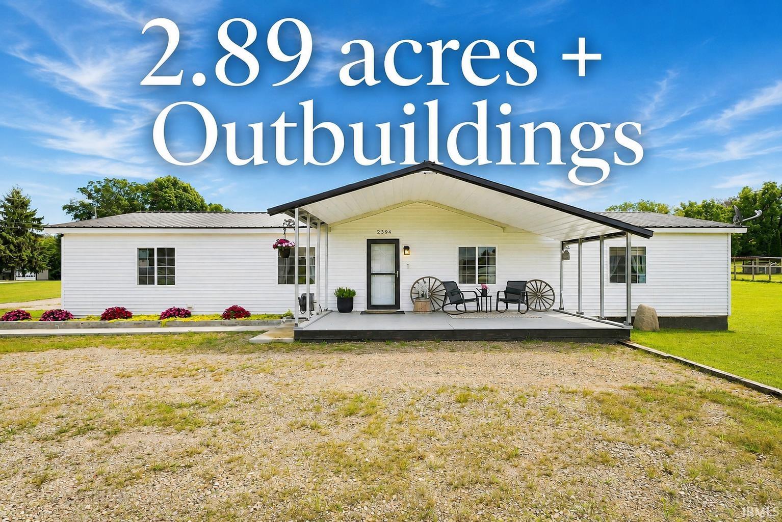 White single-story home with a broad covered porch, wagon wheels, flower beds, and gravel drive.