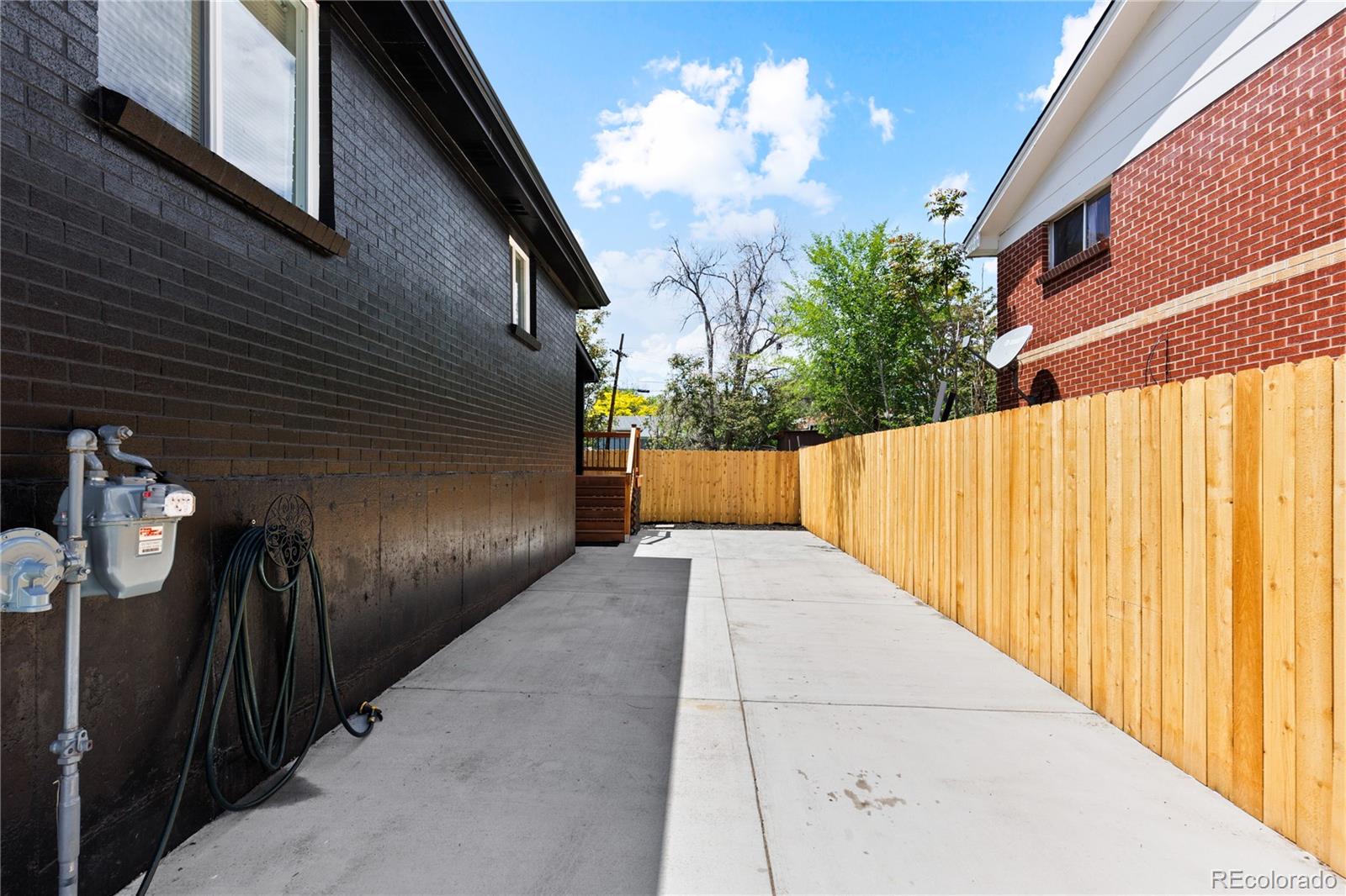Paved side patio between brick homes, enclosed by a tall wooden privacy fence.
