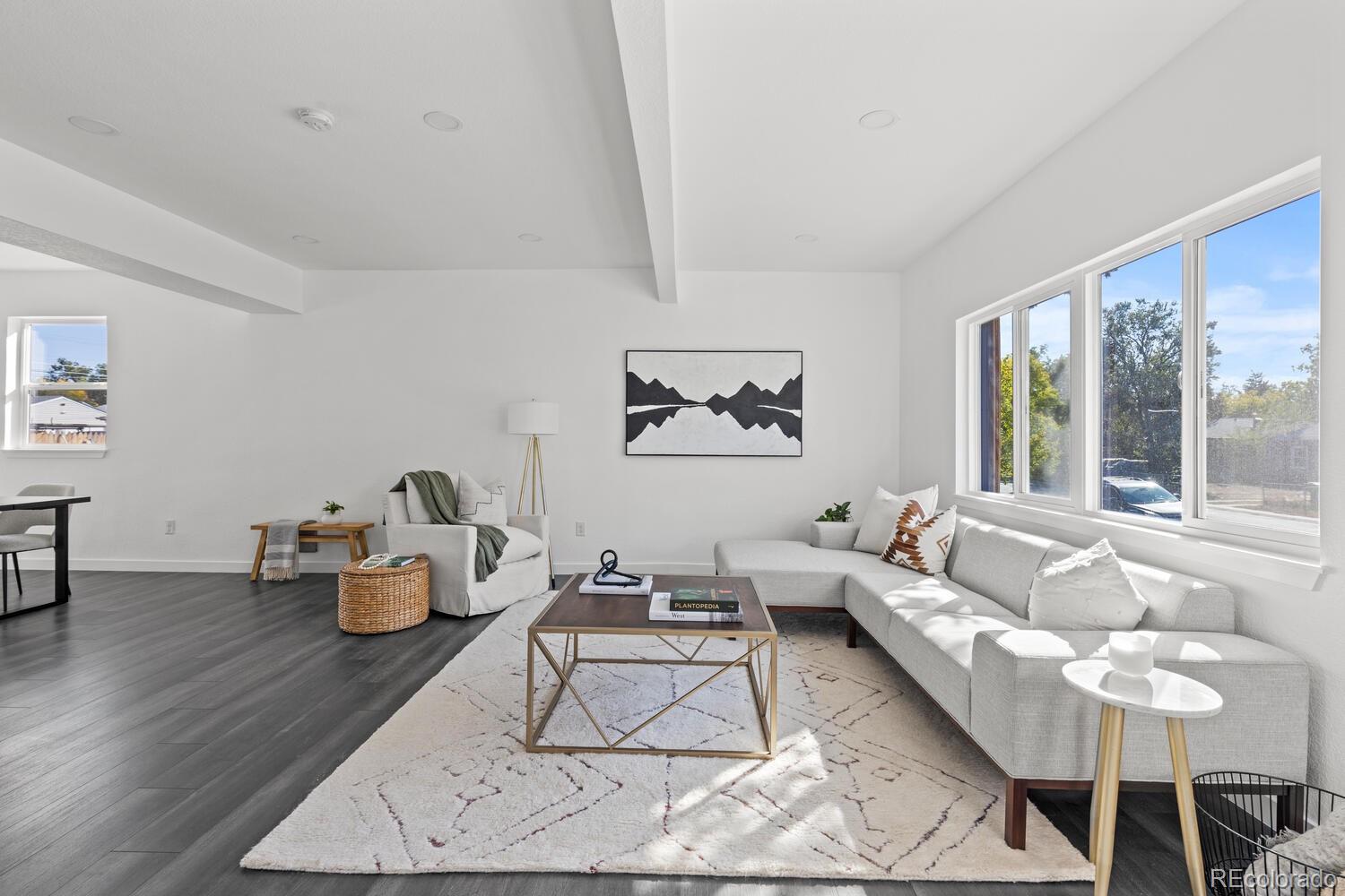 Staged living room with a light sectional, geometric rug, and large sunlit windows.