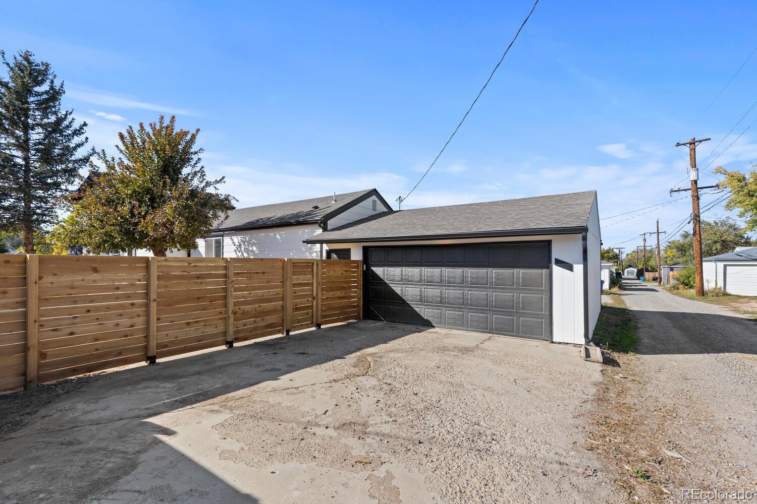 Detached white garage with a dark double door behind a wooden privacy fence.