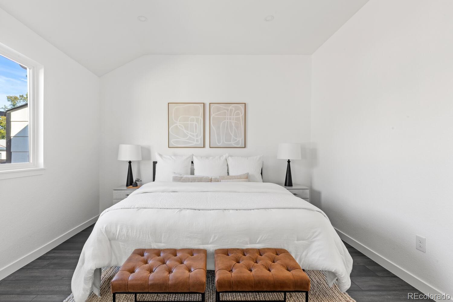 Staged bedroom with a white bed, paired brown leather benches, and abstract art above the headboard.