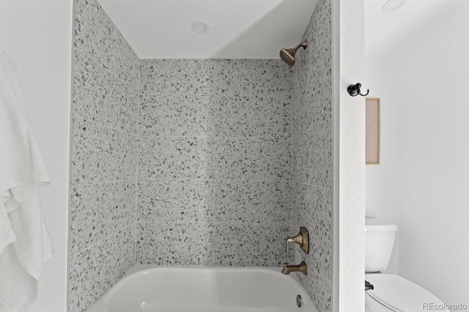 Bathroom tub and shower with terrazzo-pattern tile and bronze fixtures.