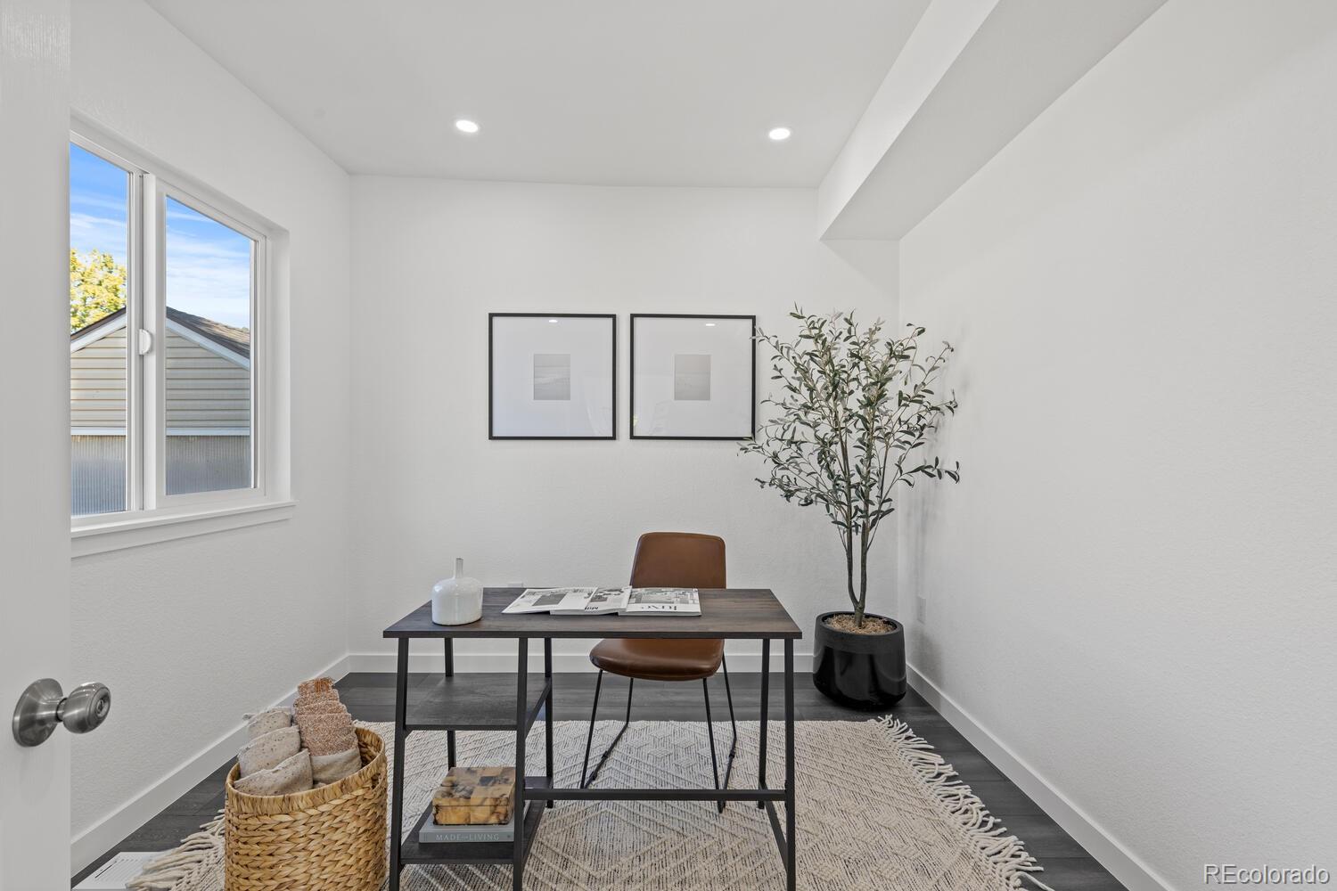 Staged home office with a dark desk, brown chair, potted tree, and window.