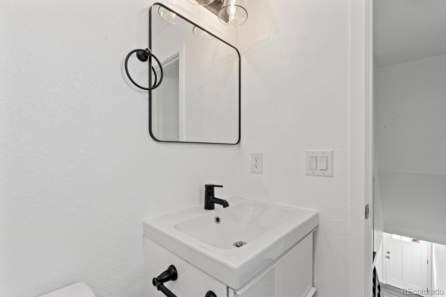 Bathroom vanity with a white sink, black faucet, and black-framed mirror.